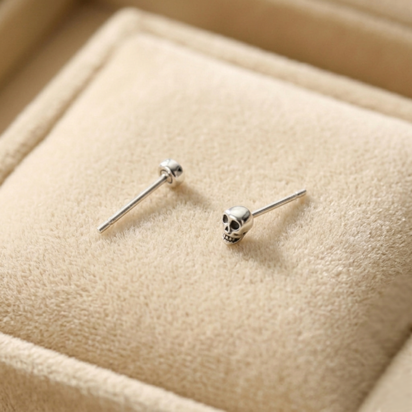 Mini gothic skull stud earrings on light fabric; silver-tone with black eye inlays