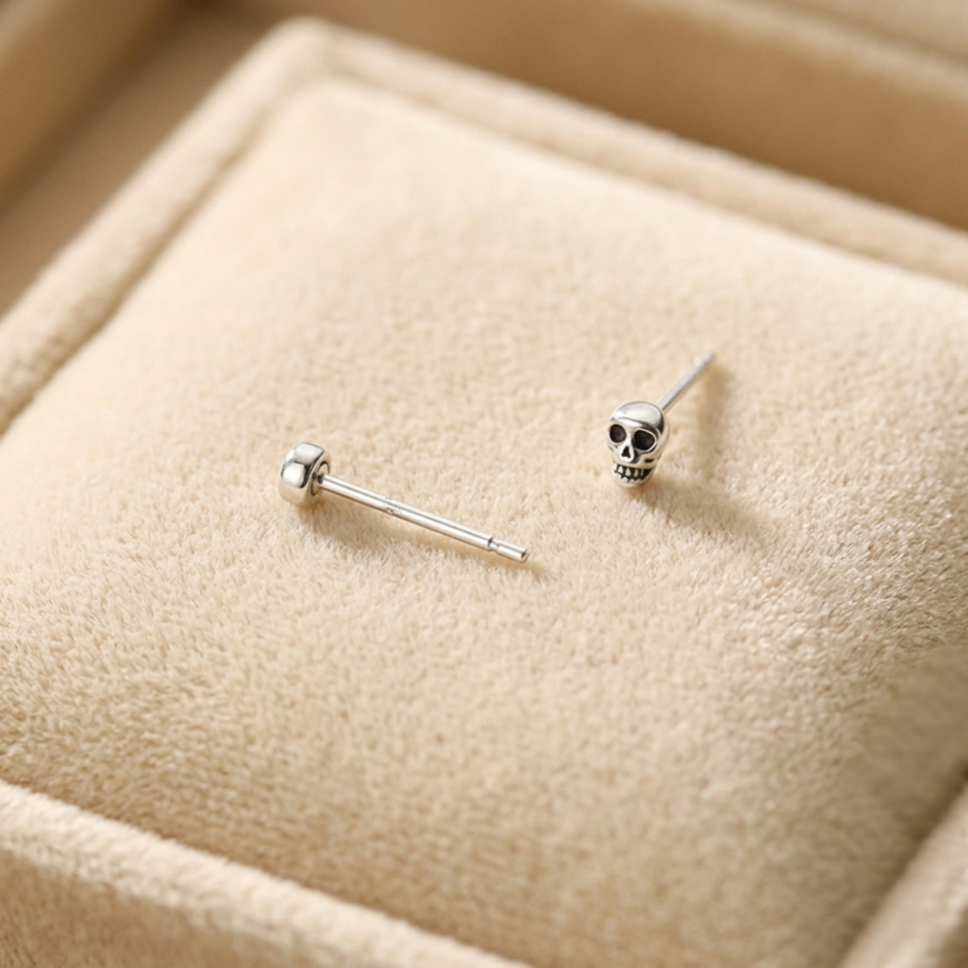 Mini gothic skull stud earrings, one front view with black-eyed skull, silver-tone post