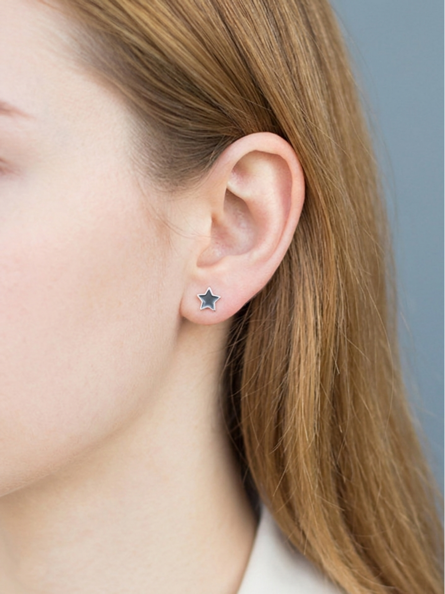 Black star stud earrings on ear, small silver star with dark enamel center