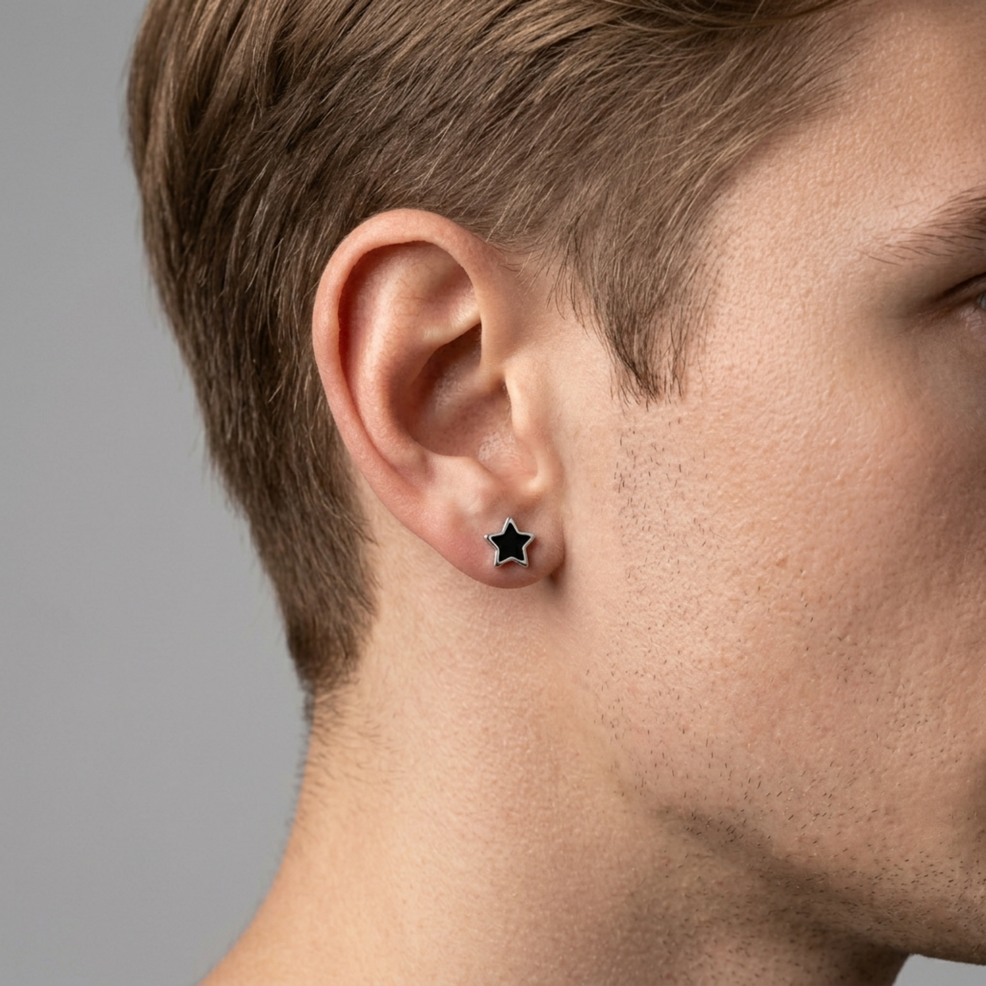 Black star stud earrings on man’s ear, silver star with dark enamel front