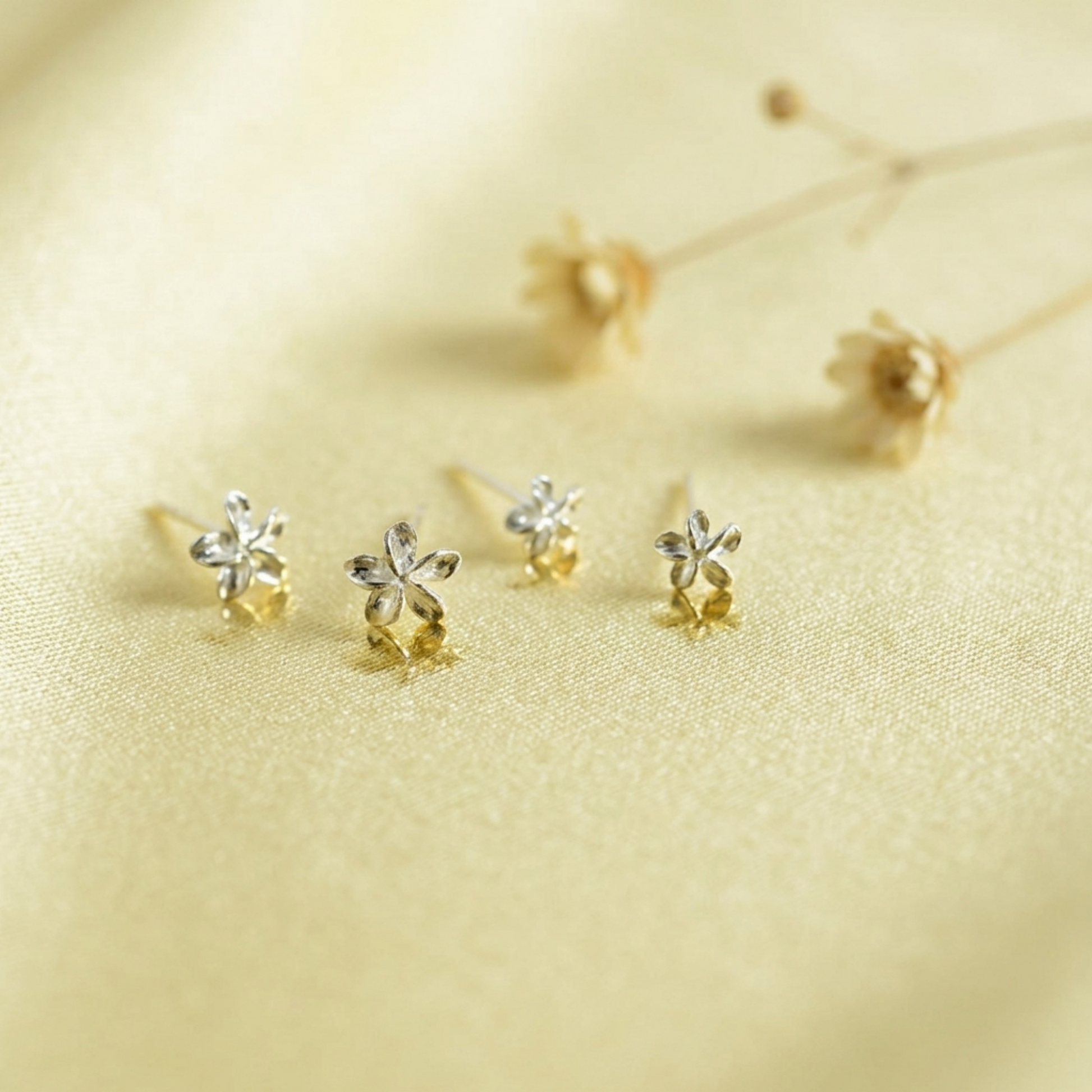 Silver lily flower stud earrings on light gold fabric