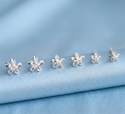 Silver lily flower stud earrings arranged on light blue fabric