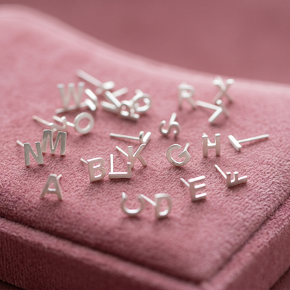Assorted initial stud earrings with silver-tone letters, scattered on fabric