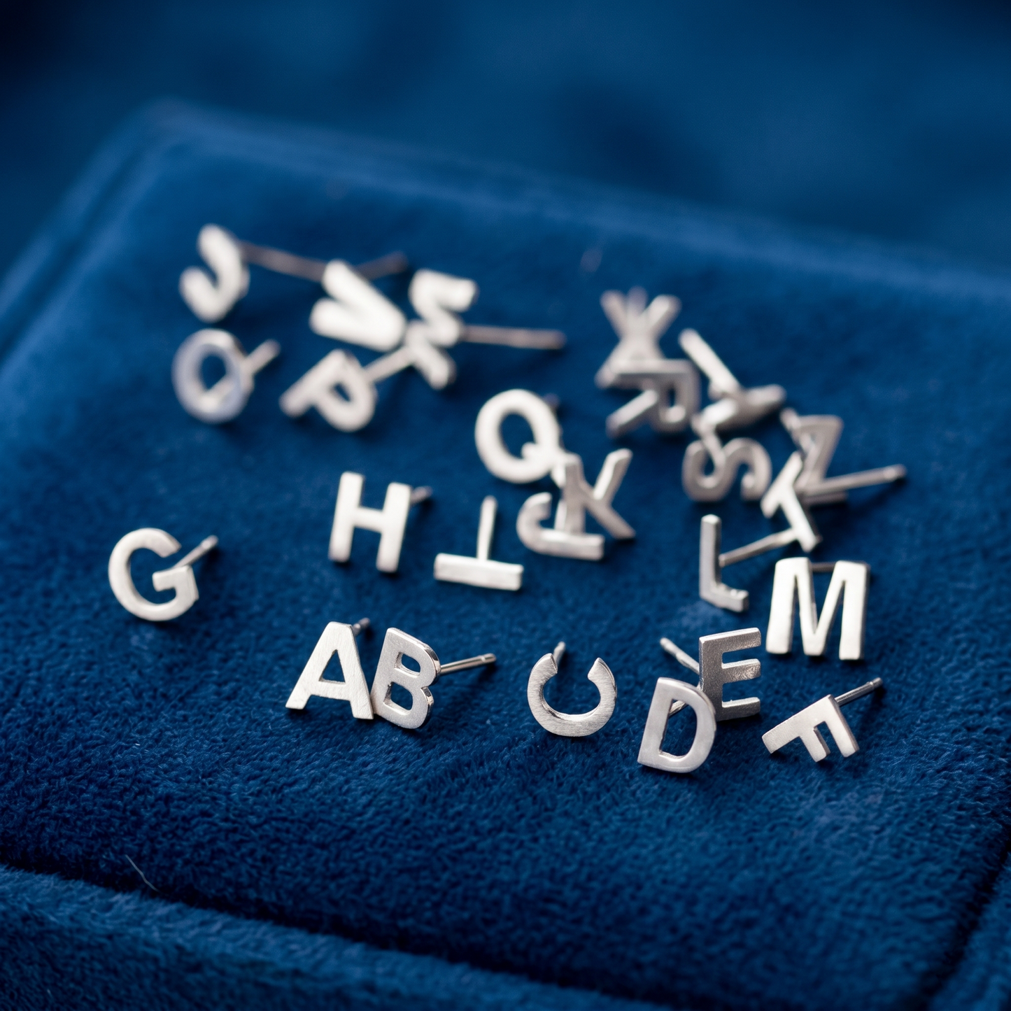 Silver-tone initial stud earrings with letters, assorted pairs on blue fabric