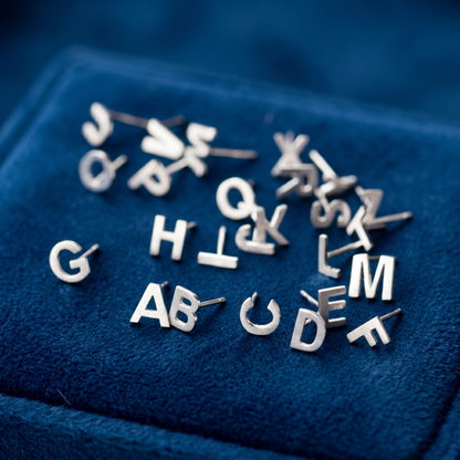 Silver-tone initial stud earrings with letters, assorted pairs on blue fabric