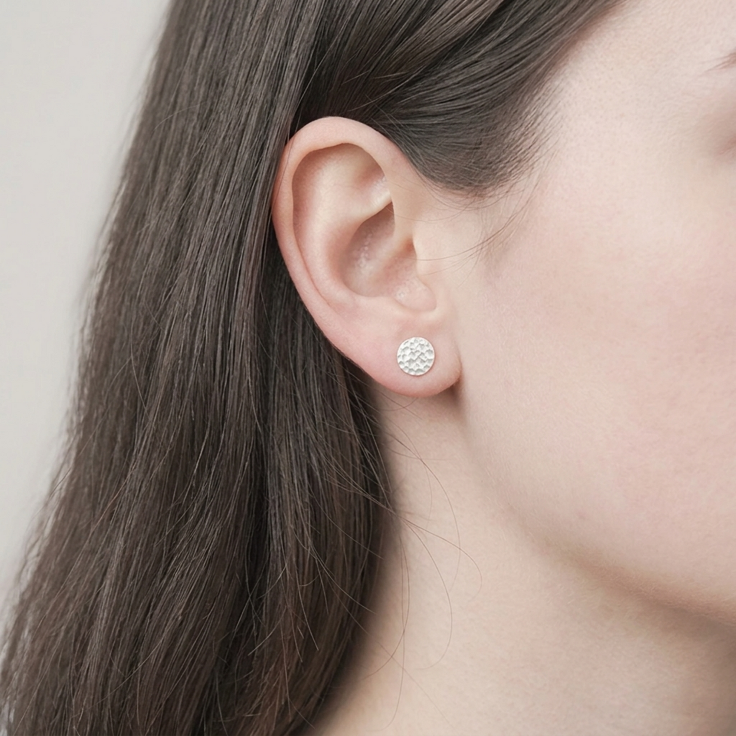 Hammered disc stud earring worn on ear, small textured round silver-tone