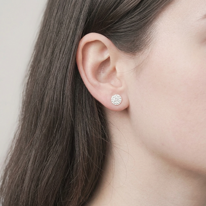Hammered disc stud earring worn on ear, small textured round silver-tone