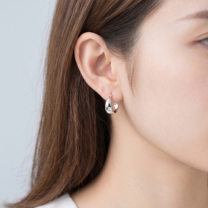 Silver wide dome huggie hoop earrings worn on ear, angled close view