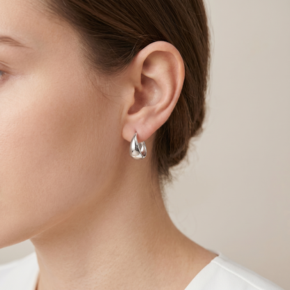 Silver wide dome huggie hoop earrings worn on ear, front view