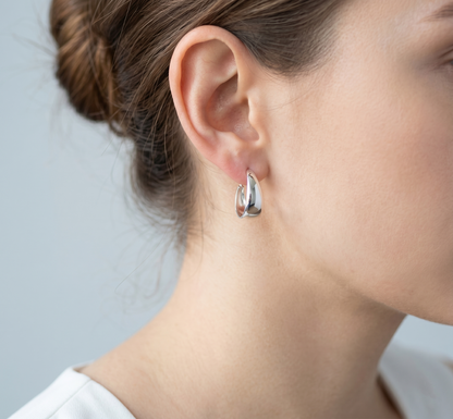 Silver wide dome huggie hoop earrings worn on ear, side view