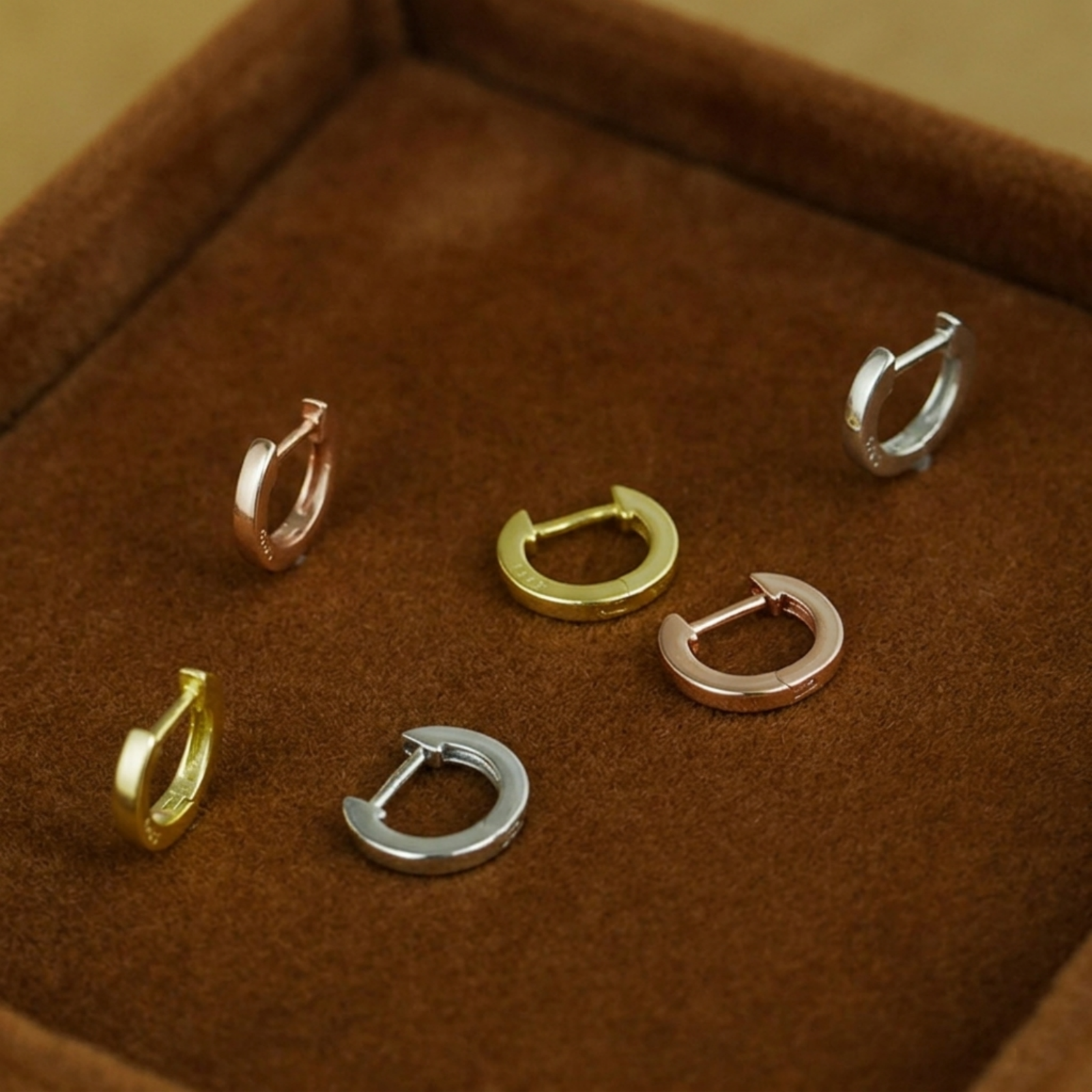 Assorted latch-back hoop earrings laid in a jewelry box, multiple metal tones