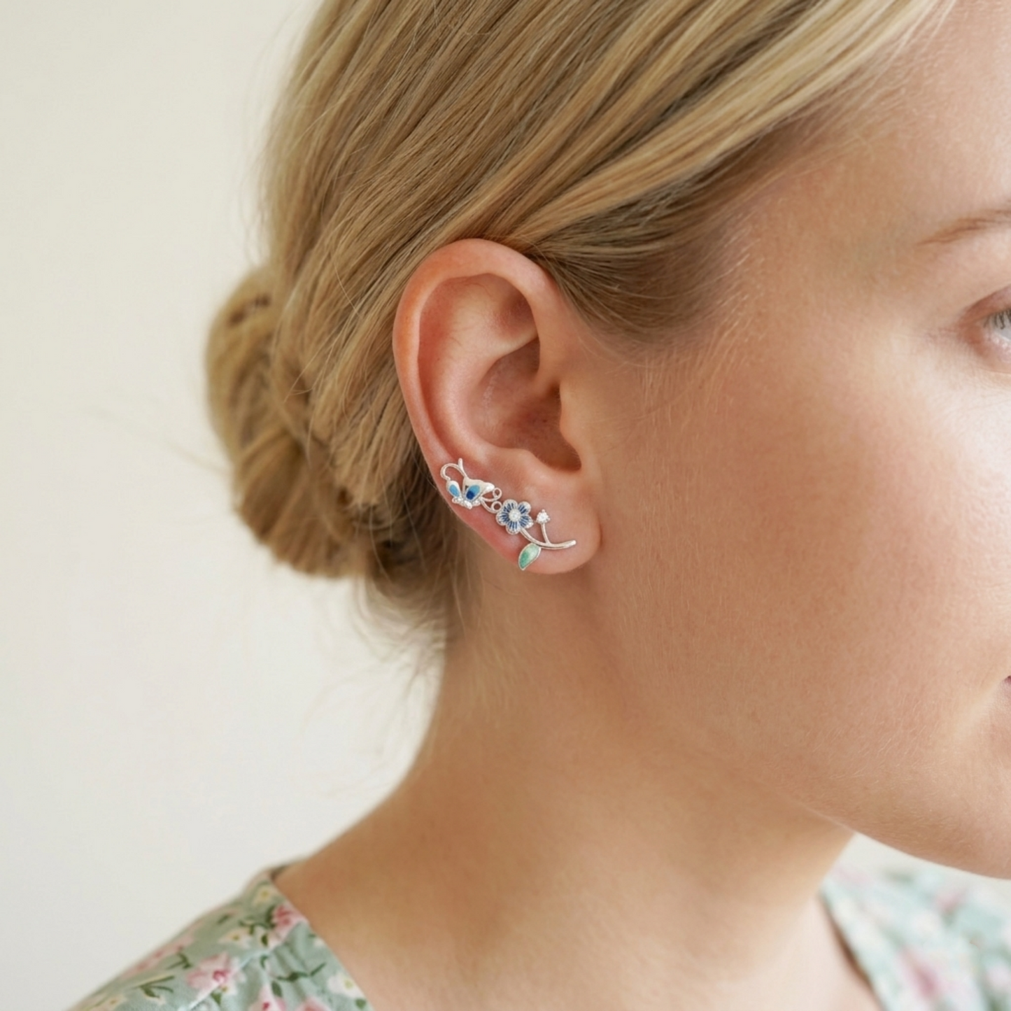 Butterfly climber earrings worn on ear; blue enamel butterfly with crystal flower details.