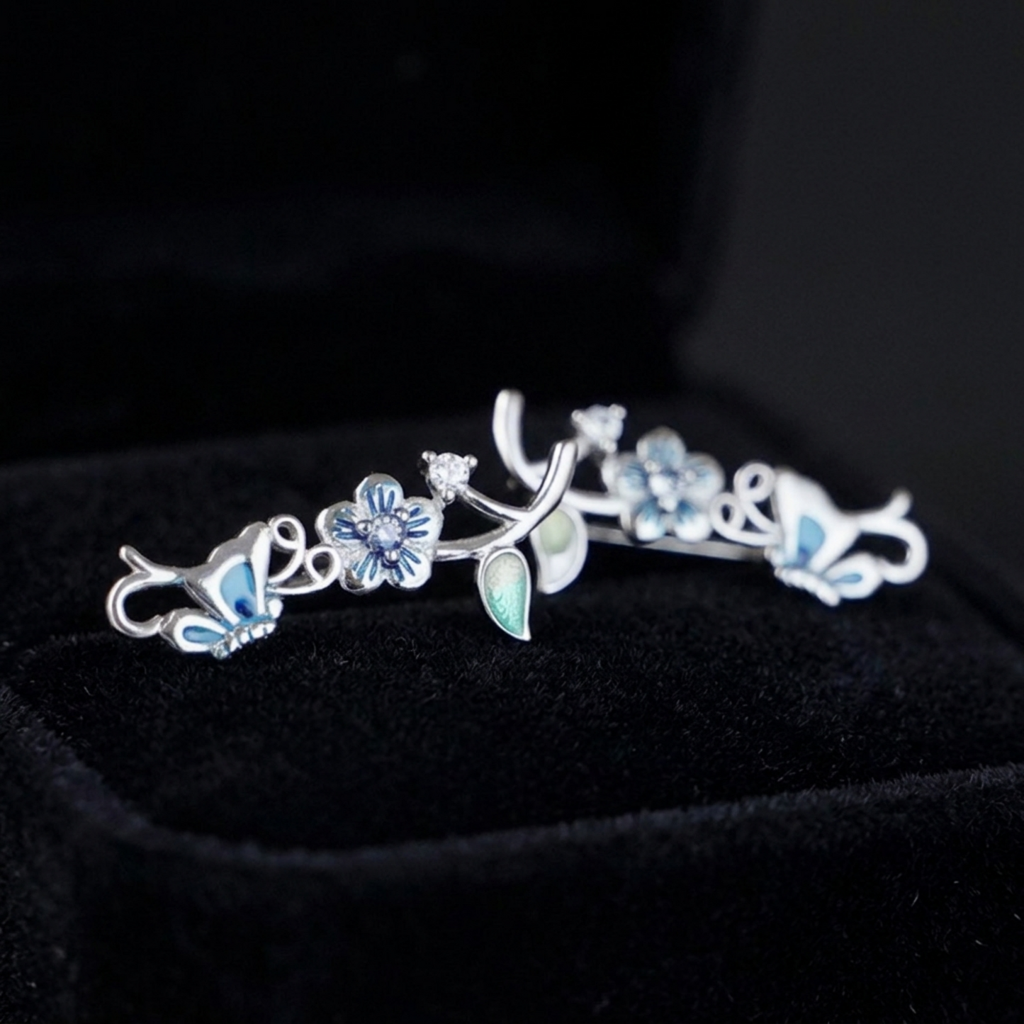 Butterfly climber earrings close-up with blue and green enamel leaves, crystal flower accents.