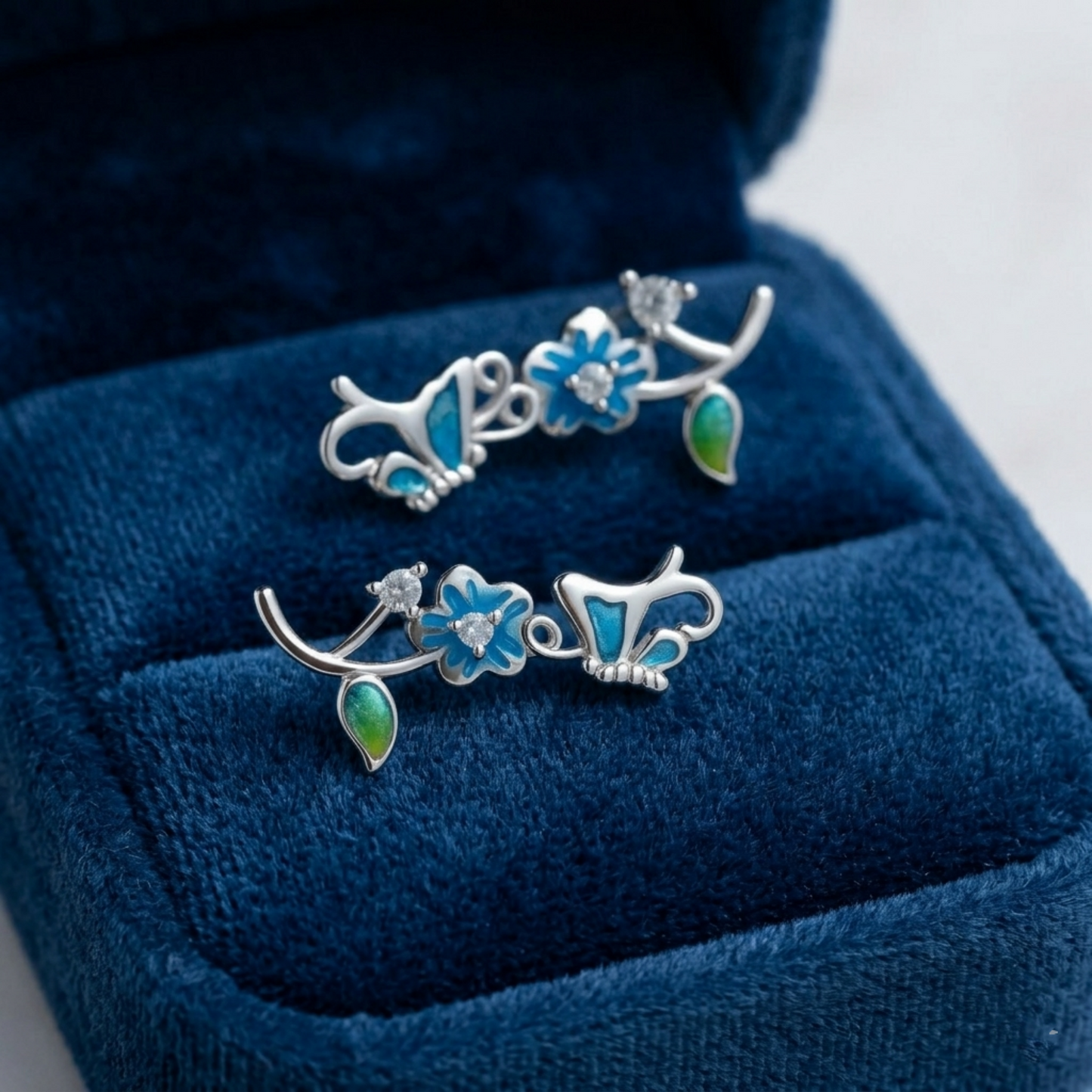 Butterfly climber earrings on display with blue enamel butterflies and green enamel drop pieces.
