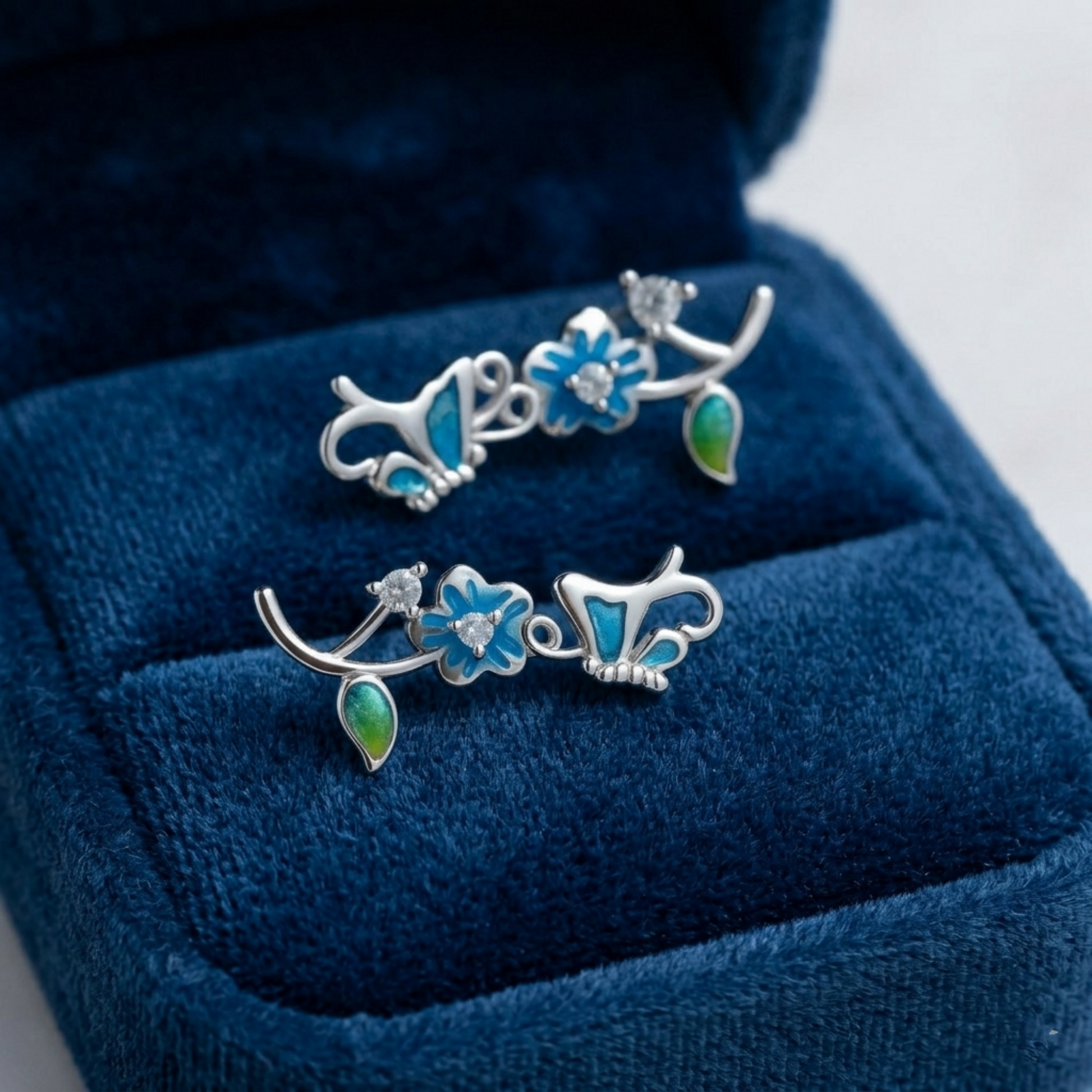 Butterfly climber earrings on display with blue enamel butterflies and green enamel drop pieces.