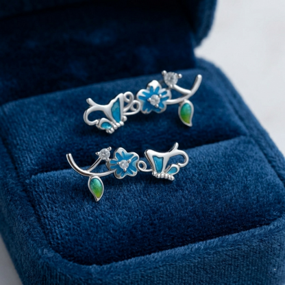Butterfly climber earrings on display with blue enamel butterflies and green enamel drop pieces.