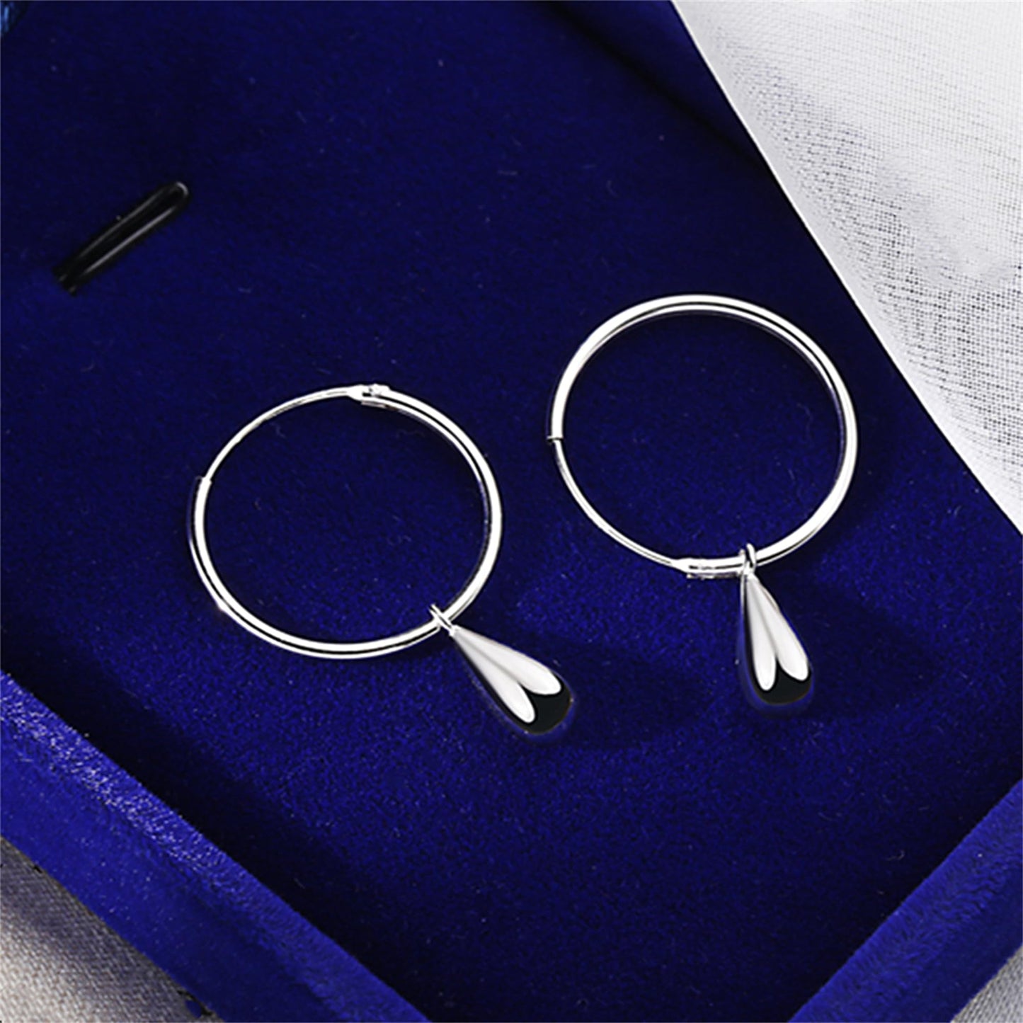 Silver teardrop hoop earrings, pair laid flat with dangling teardrop ends