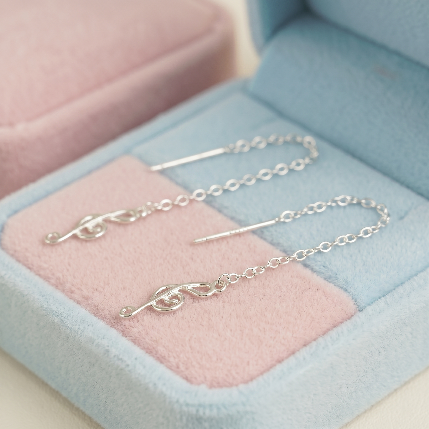 Silver treble-note dangle threader earrings laid on pink-and-blue velvet jewelry box