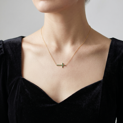 Green CZ sideways cross necklace on gold-tone chain, on collarbone