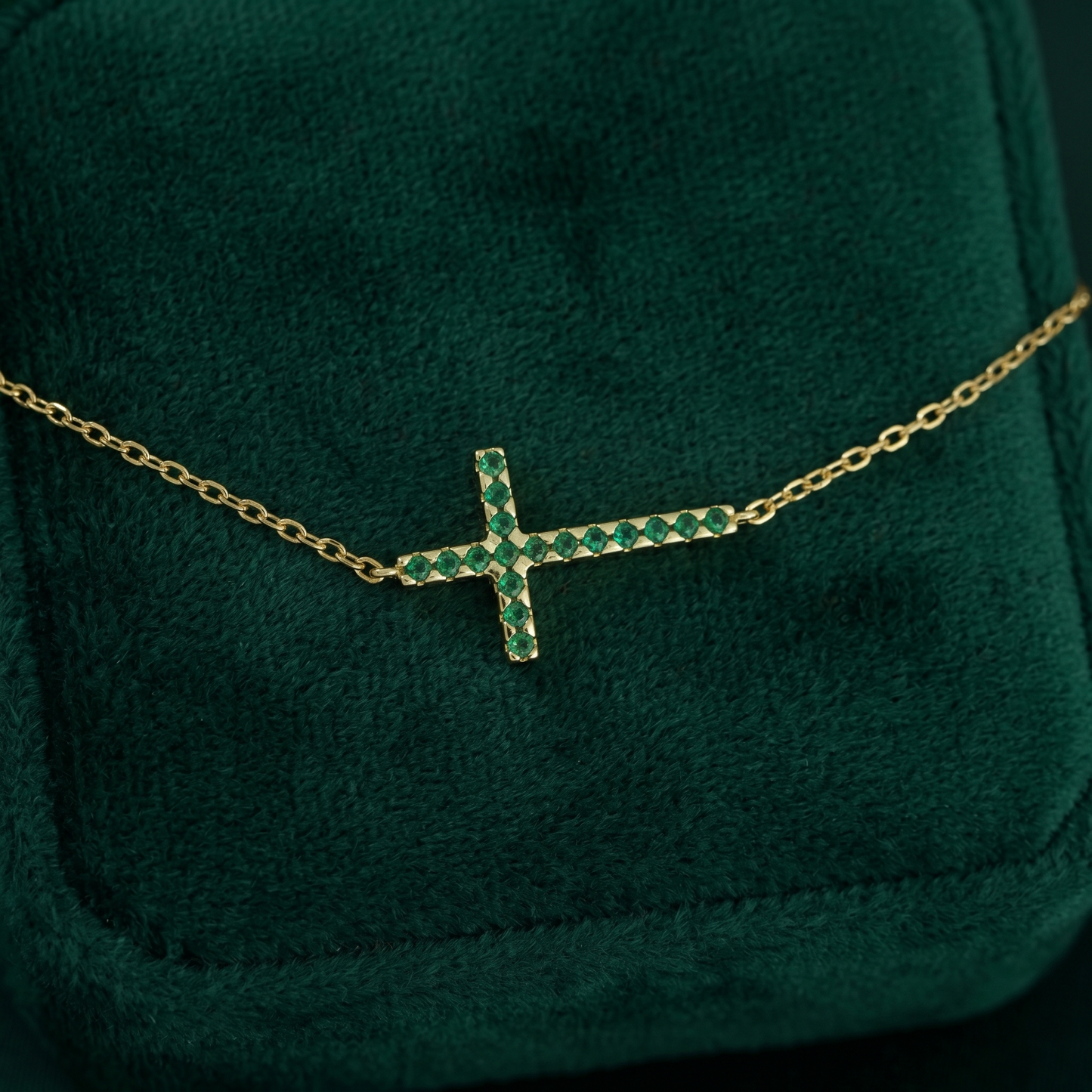 Close-up: sideways green CZ cross pendant on gold-tone chain