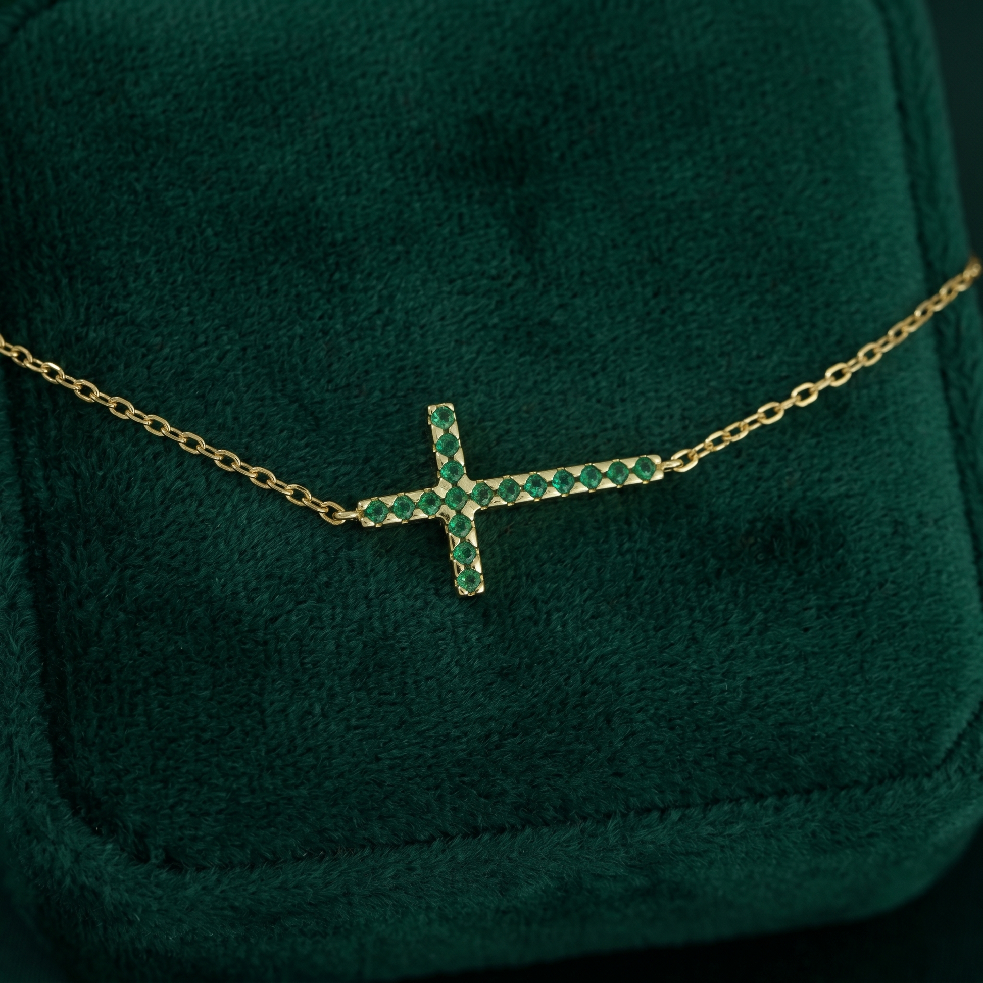 Close-up: sideways green CZ cross pendant on gold-tone chain