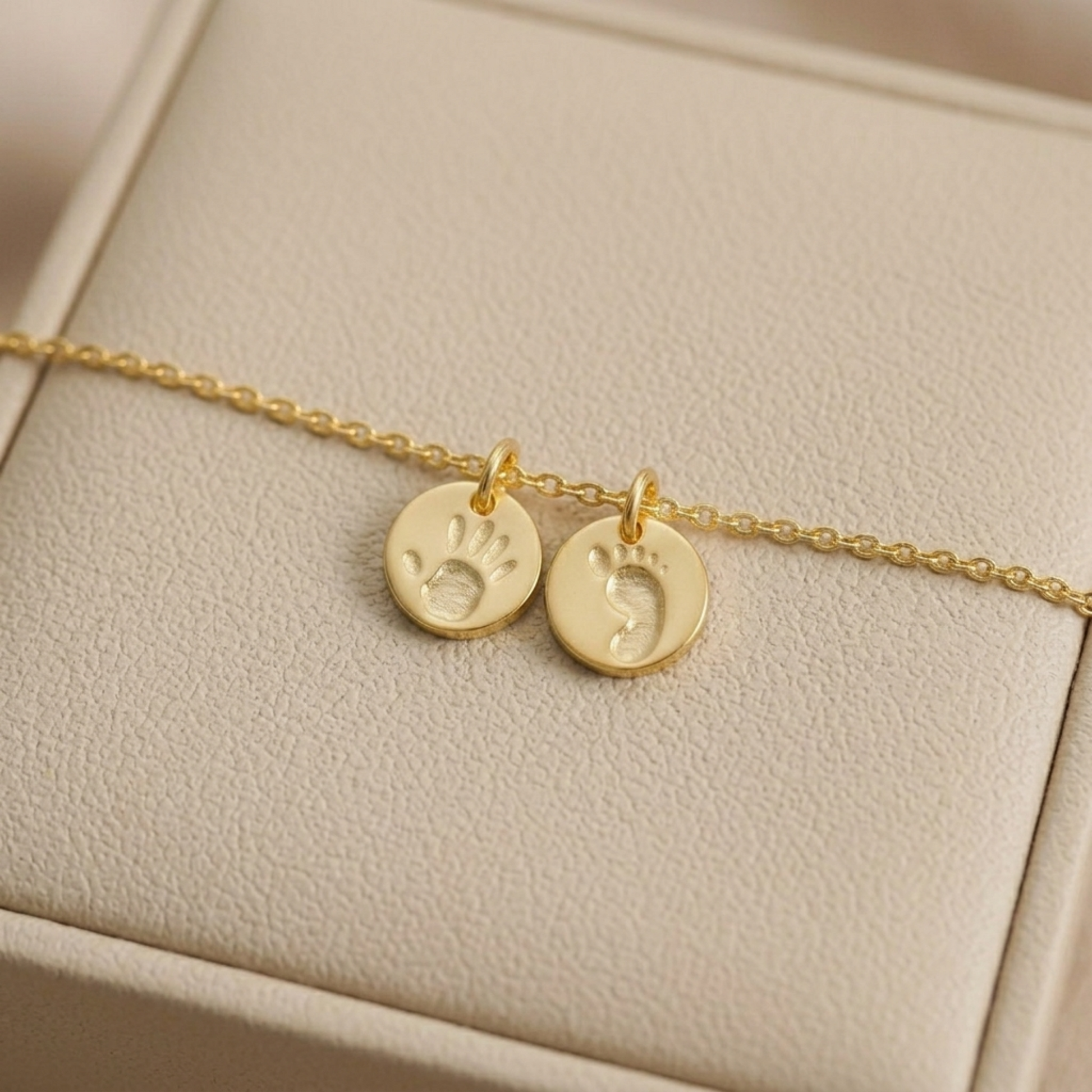 Gold round handprint and footprint charms on a thin chain