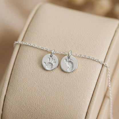 Silver round handprint and footprint charms on a thin chain
