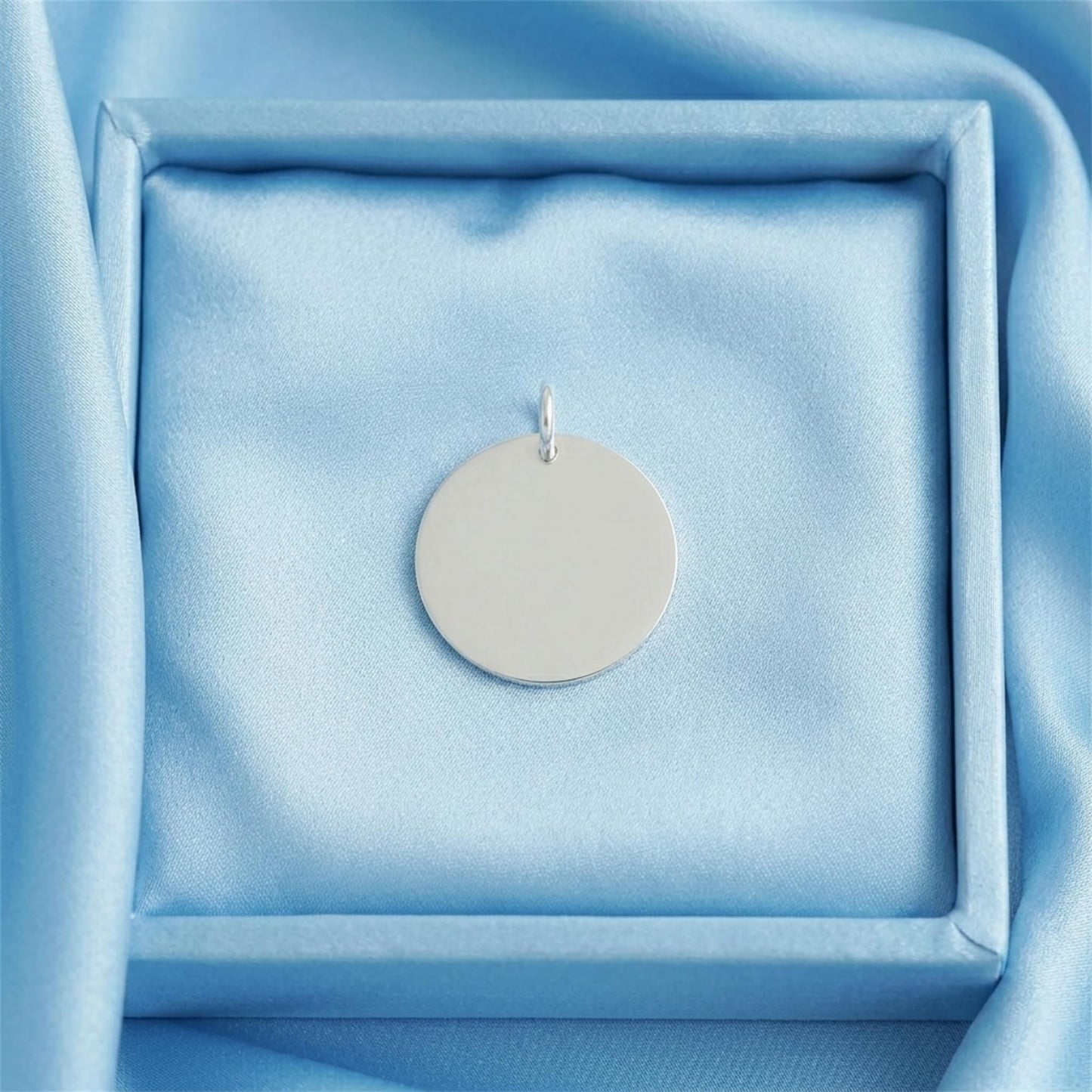 Round polished disc pendant displayed in jewelry box, silver-tone