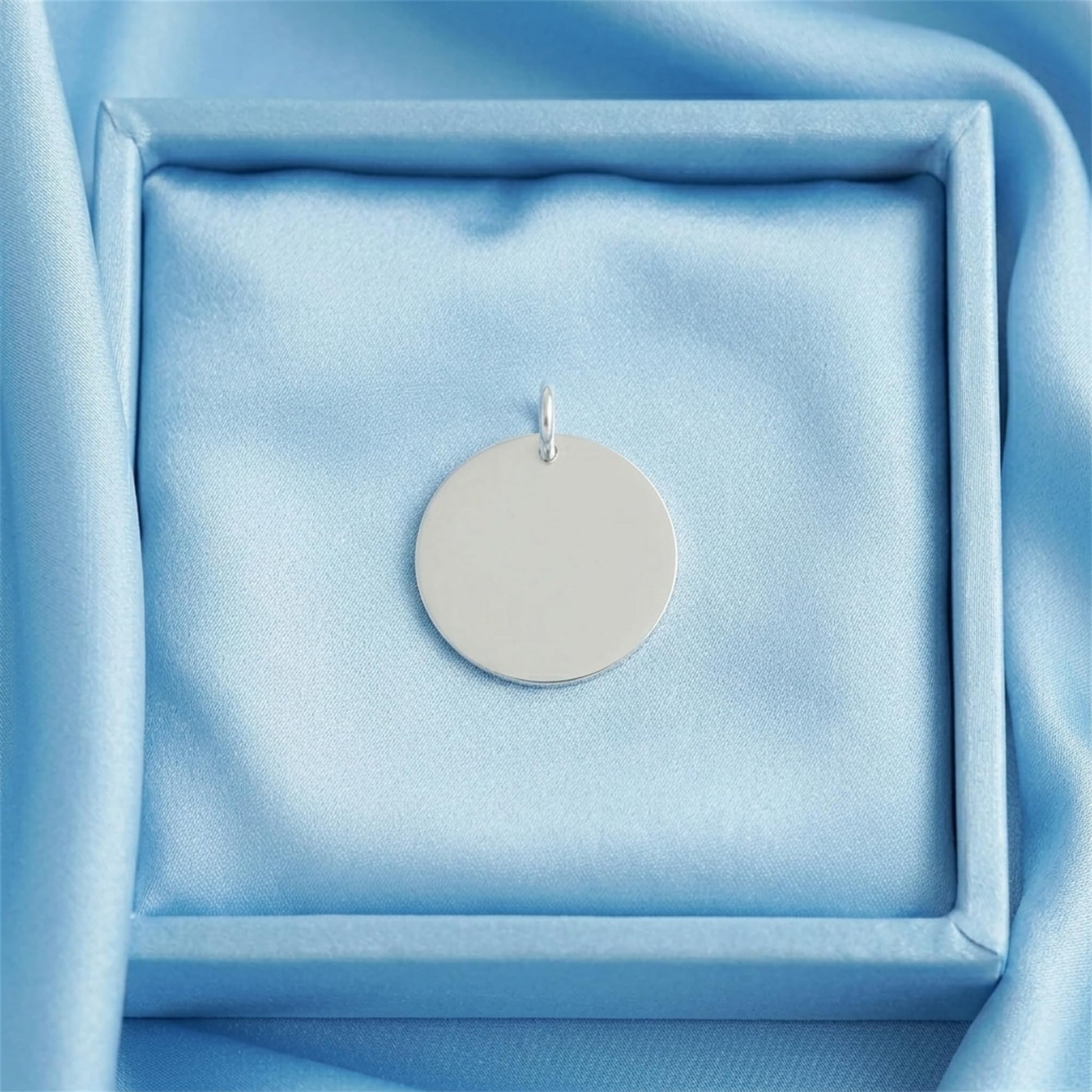 Round polished disc pendant displayed in jewelry box, silver-tone