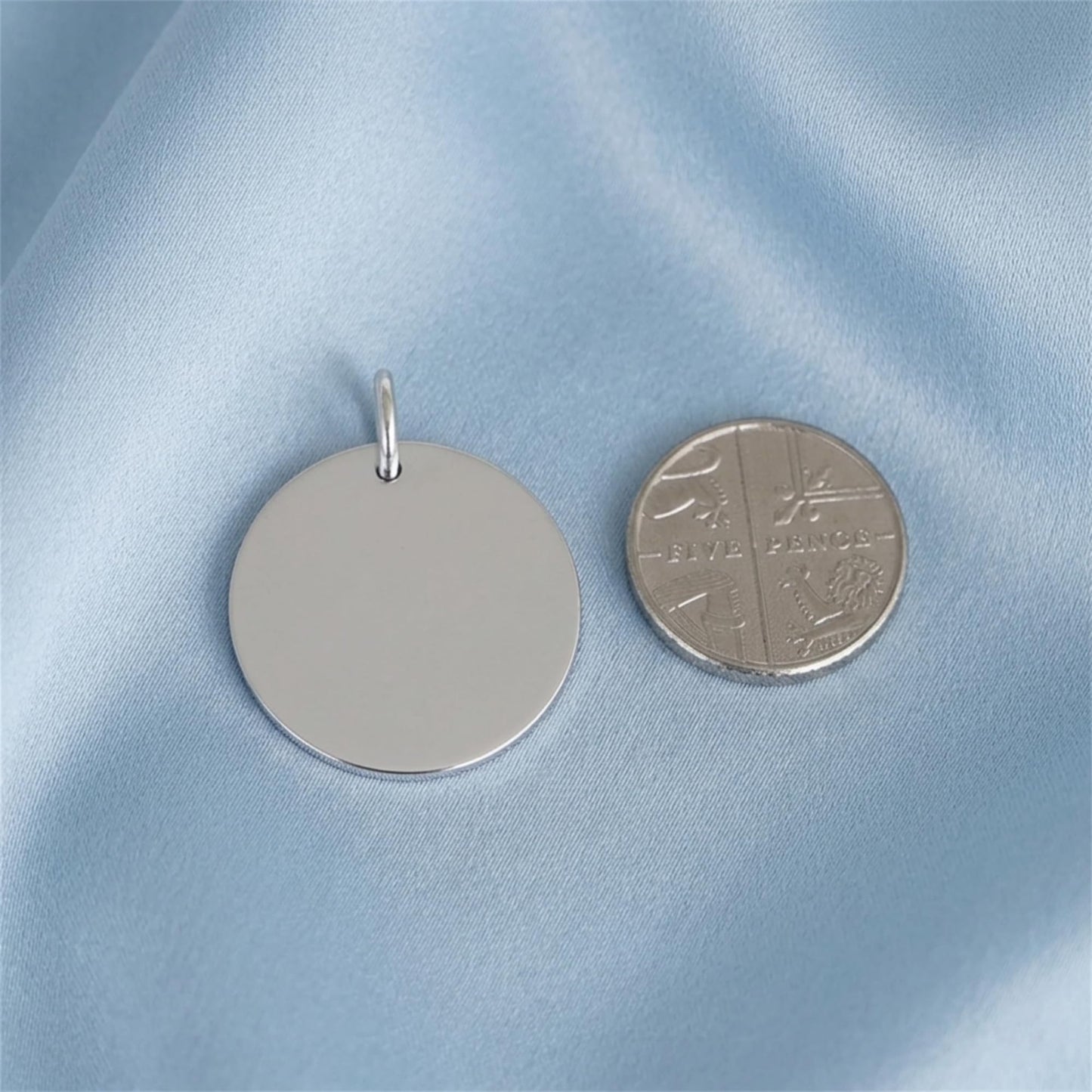 Round polished disc pendant with loop bail beside coin for scale