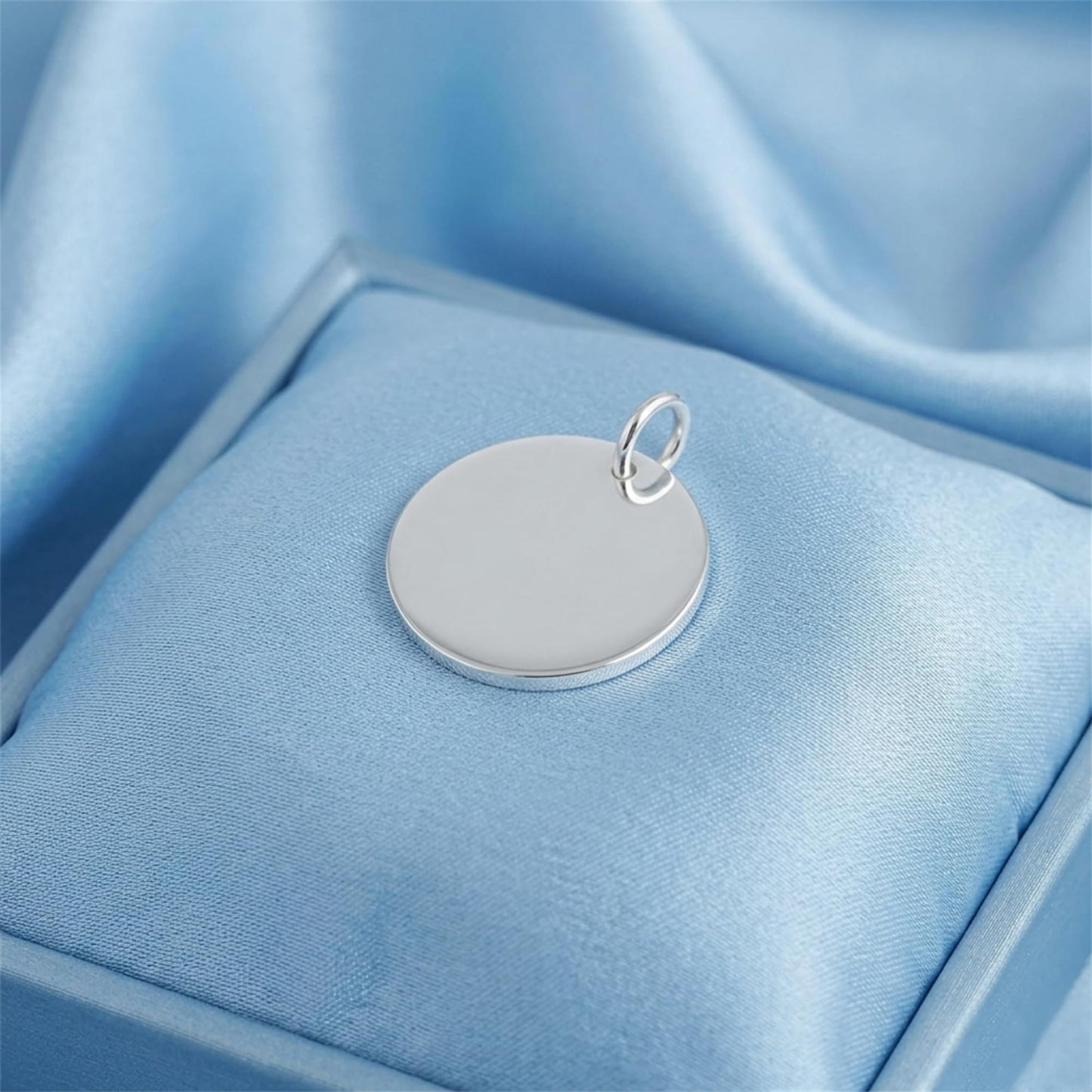 Round polished disc pendant on blue satin, silver-tone bail