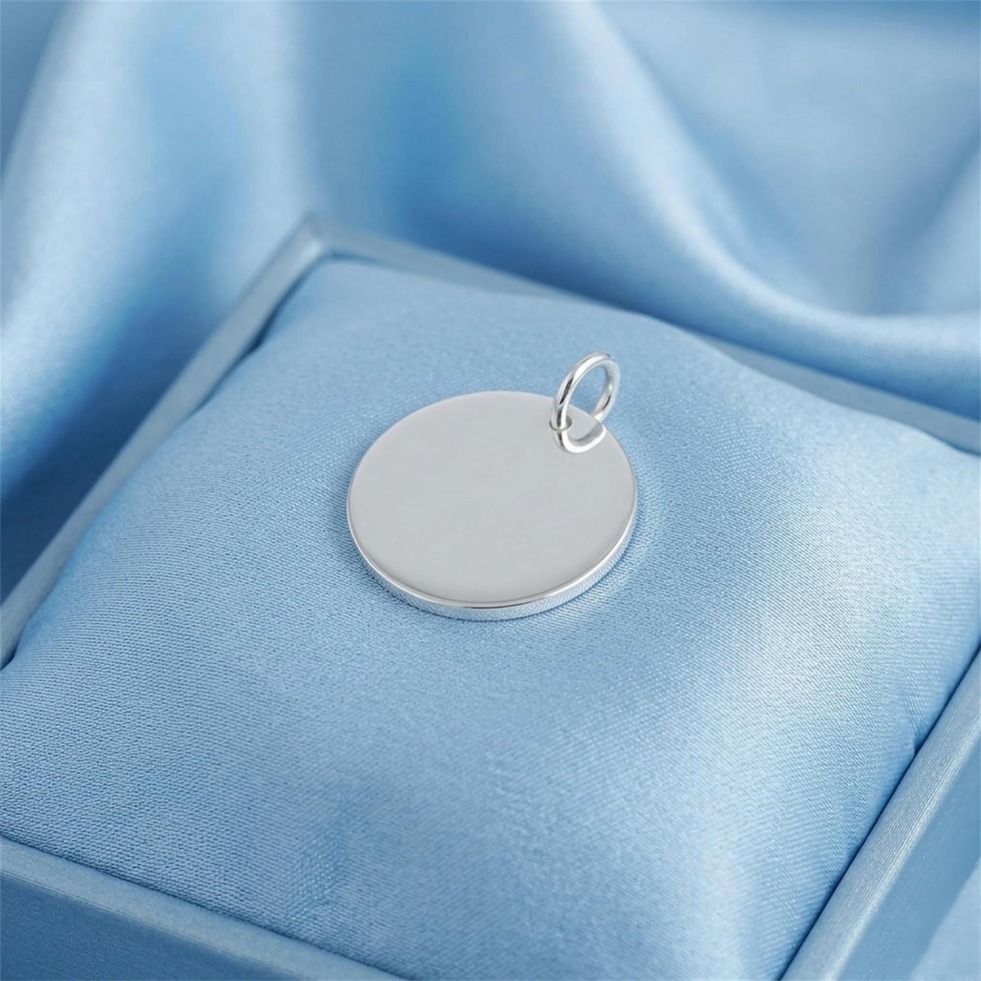 Round polished disc pendant on blue satin, silver-tone bail