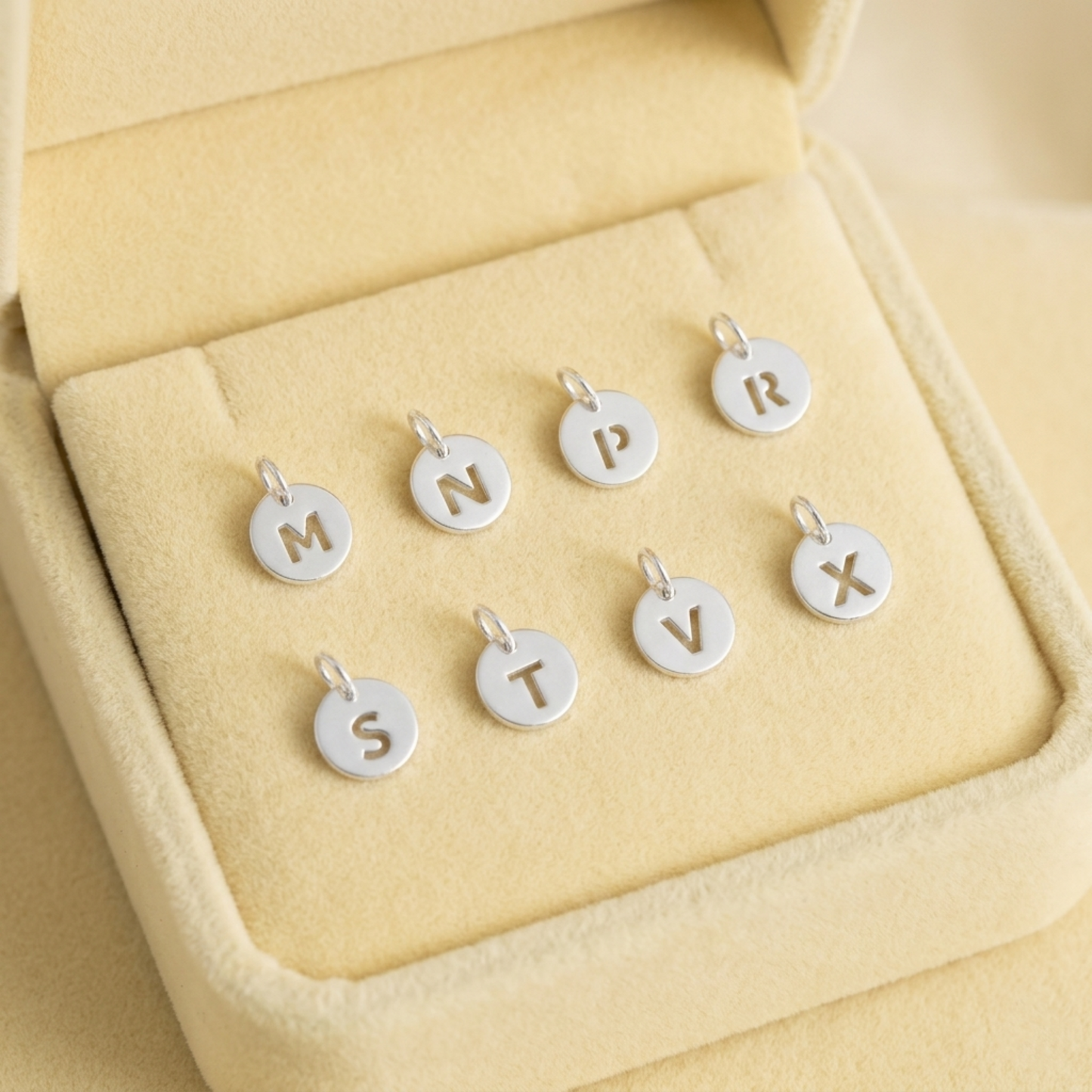 Silver hollow alphabet disc charm set with letter discs in a cream jewelry box