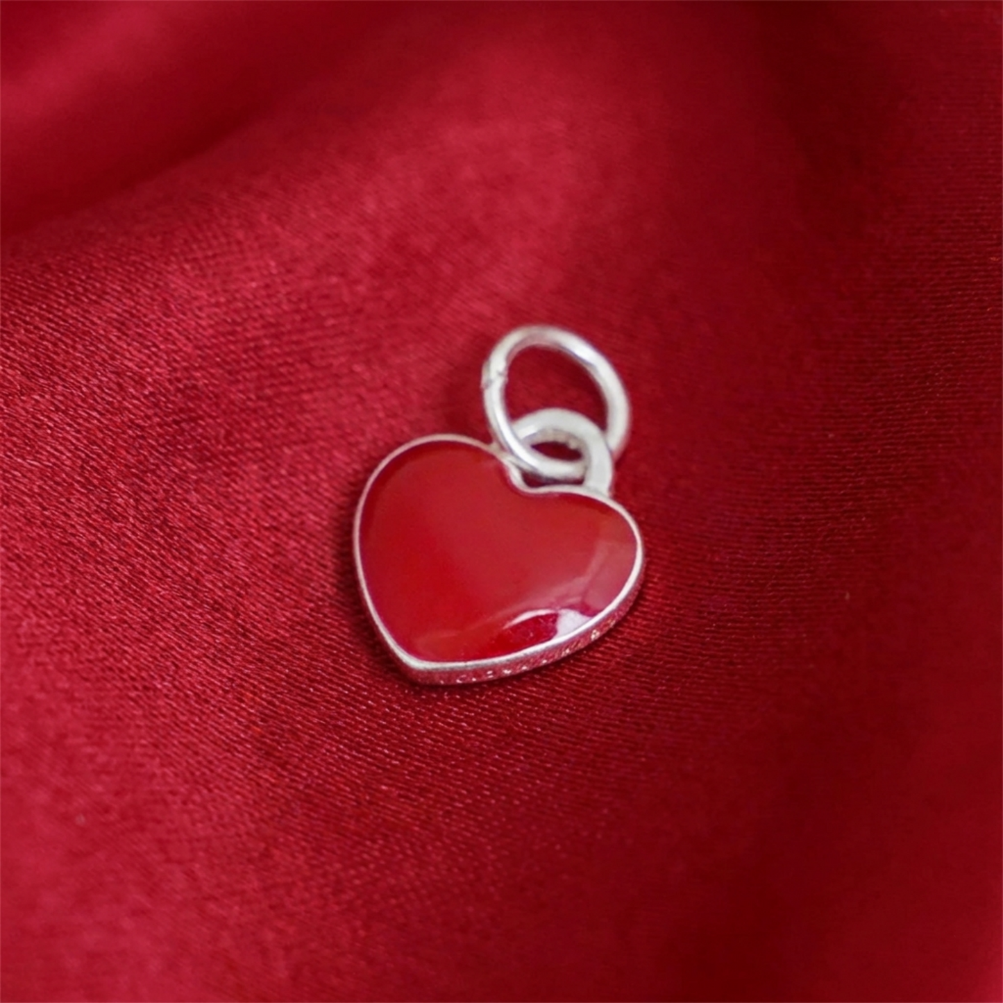 Red heart charm from side view, silver border around glossy enamel heart