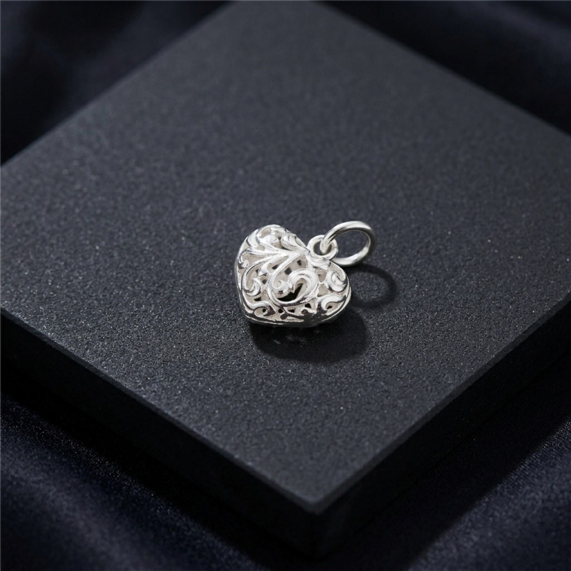 Small silver-tone filigree heart pendant on dark jewelry box