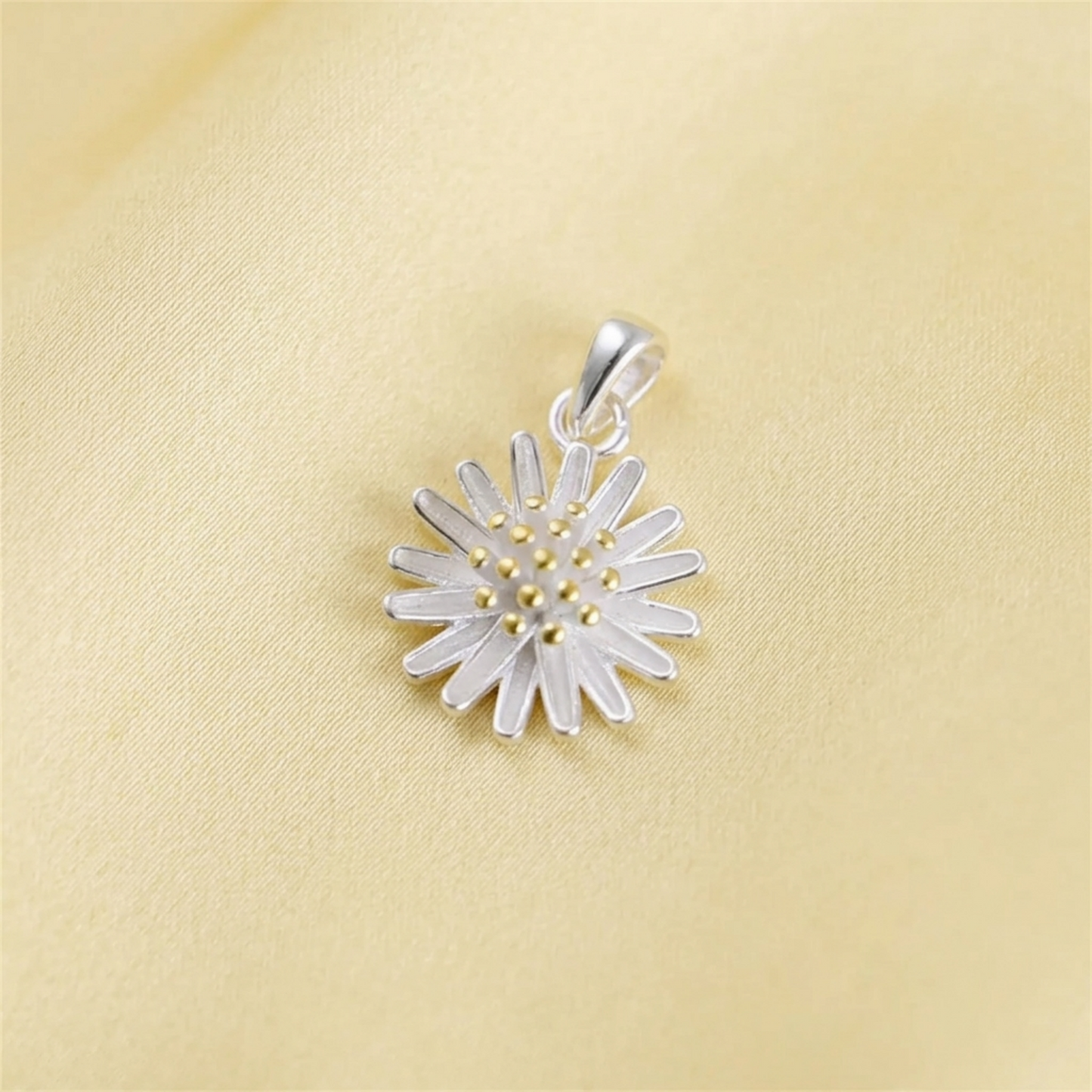 Silver daisy flower pendant with gold bead center on yellow fabric