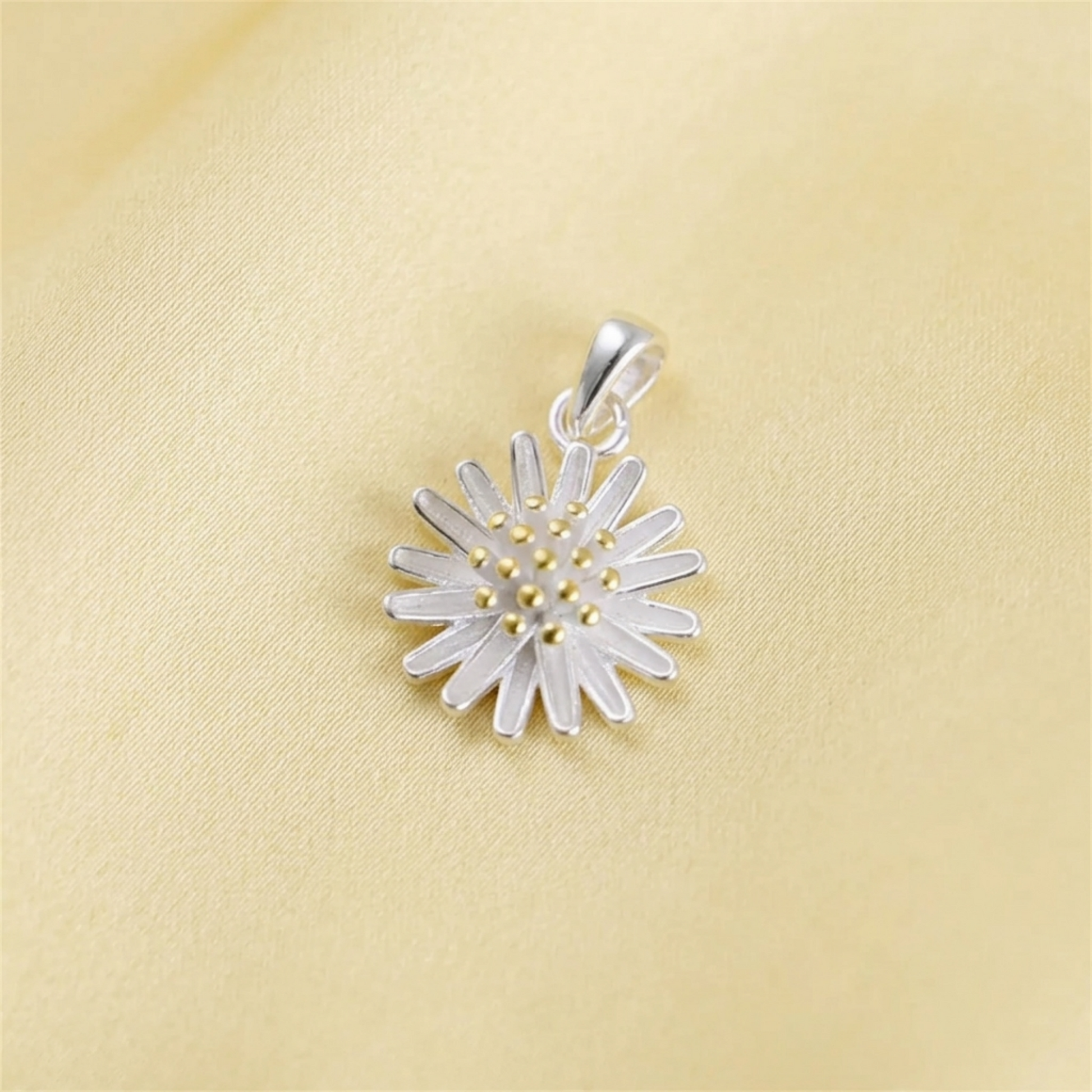 Silver daisy flower pendant with gold bead center on yellow fabric
