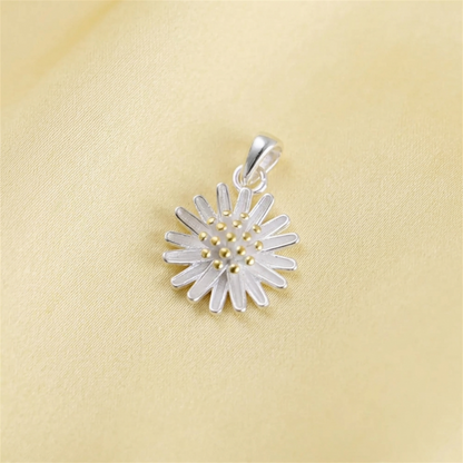 Silver daisy flower pendant with gold bead center on yellow fabric