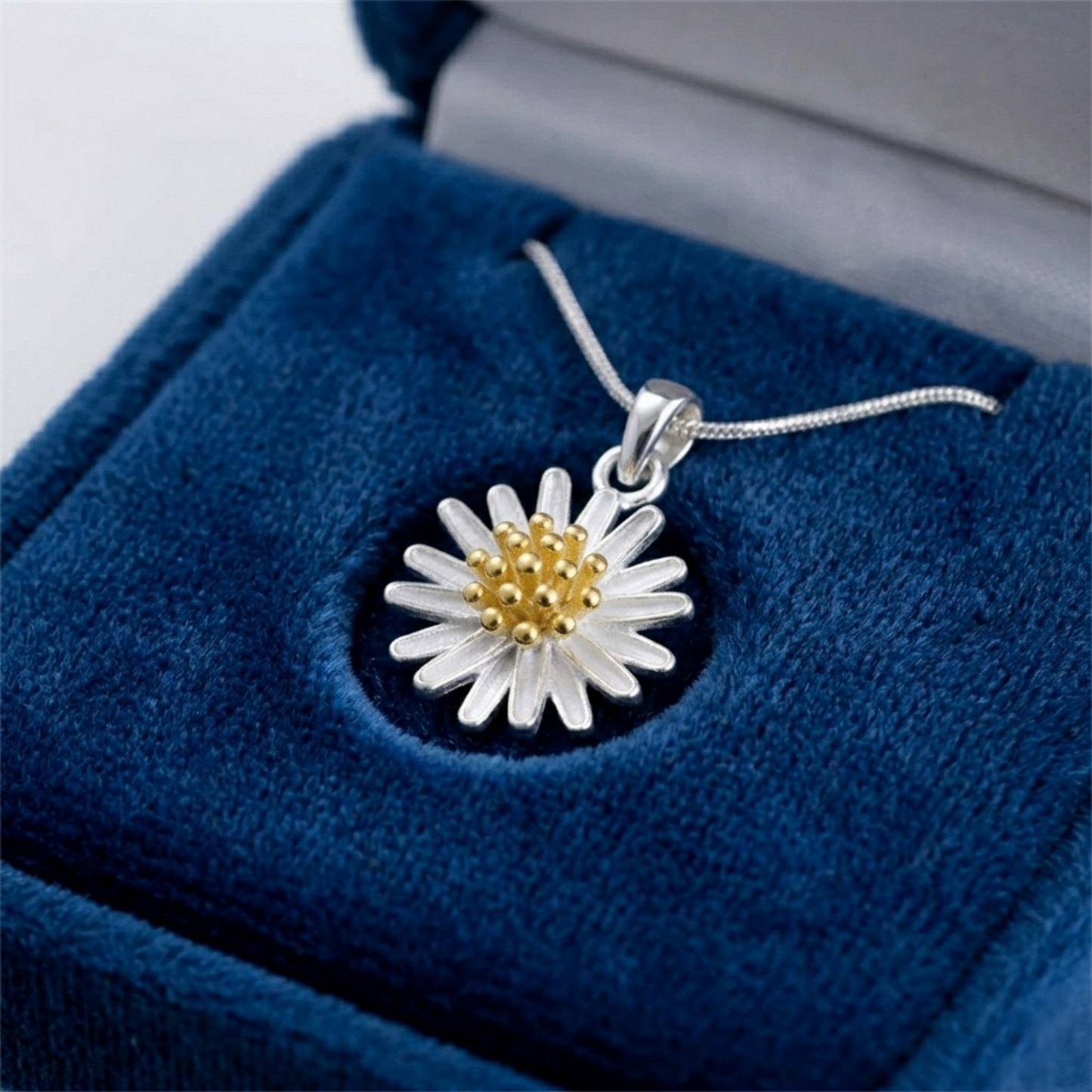 Silver daisy flower pendant with gold center on blue velvet