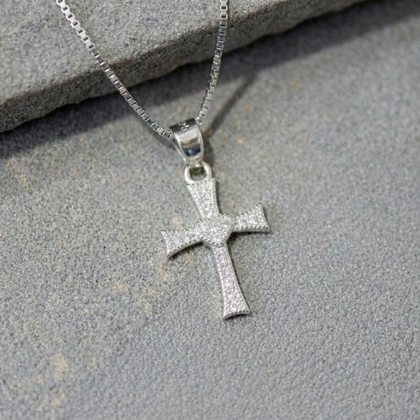 Close-up of CZ heart cross pendant, small heart at center on silver-tone cross