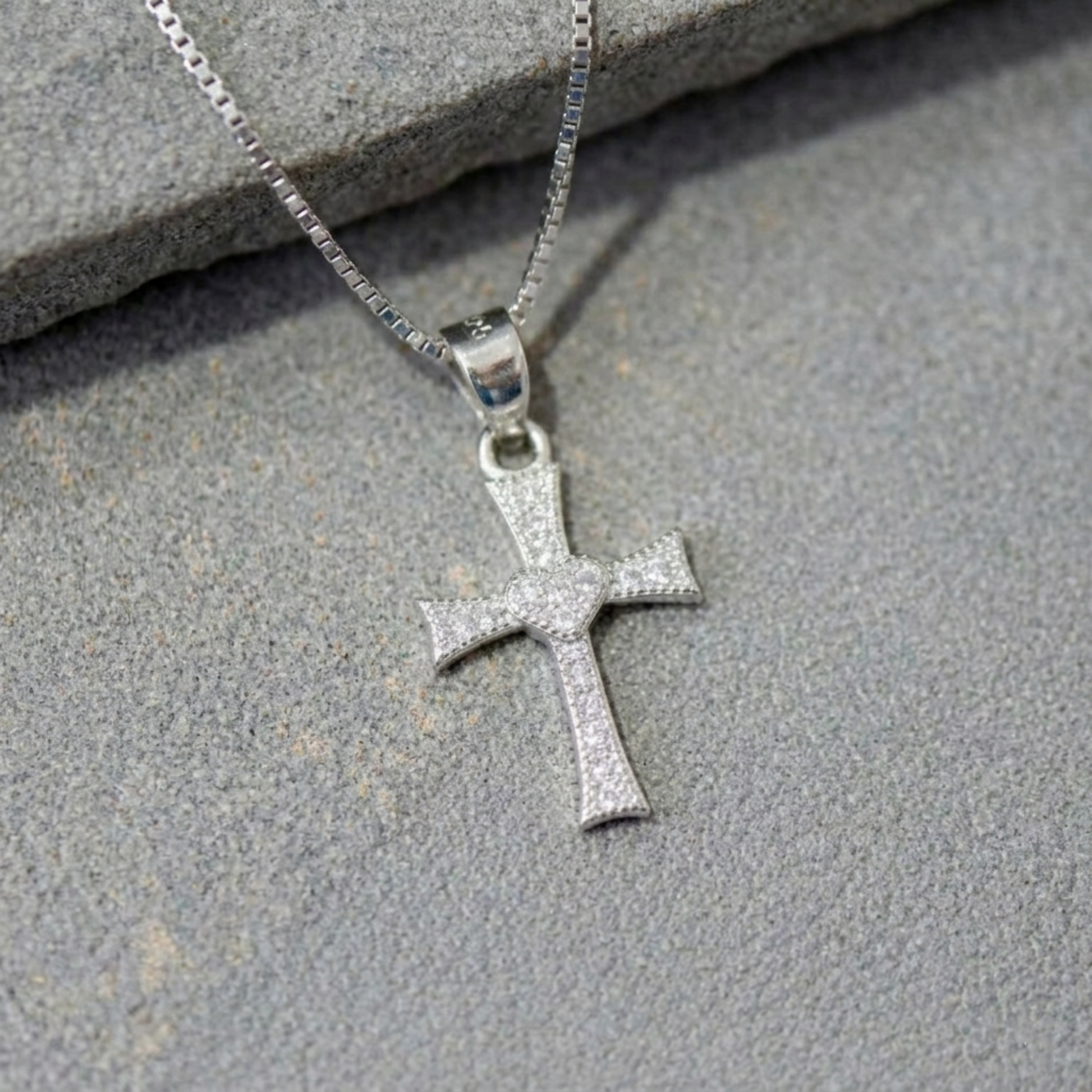 Close-up of CZ heart cross pendant, small heart at center on silver-tone cross