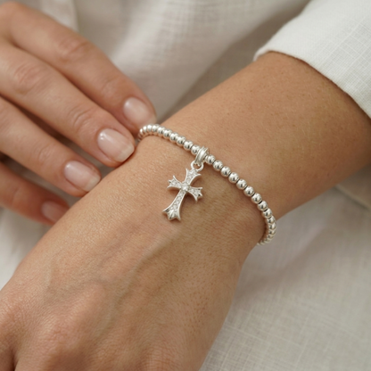 Silver CZ cross charm on a bead bracelet, shown being worn