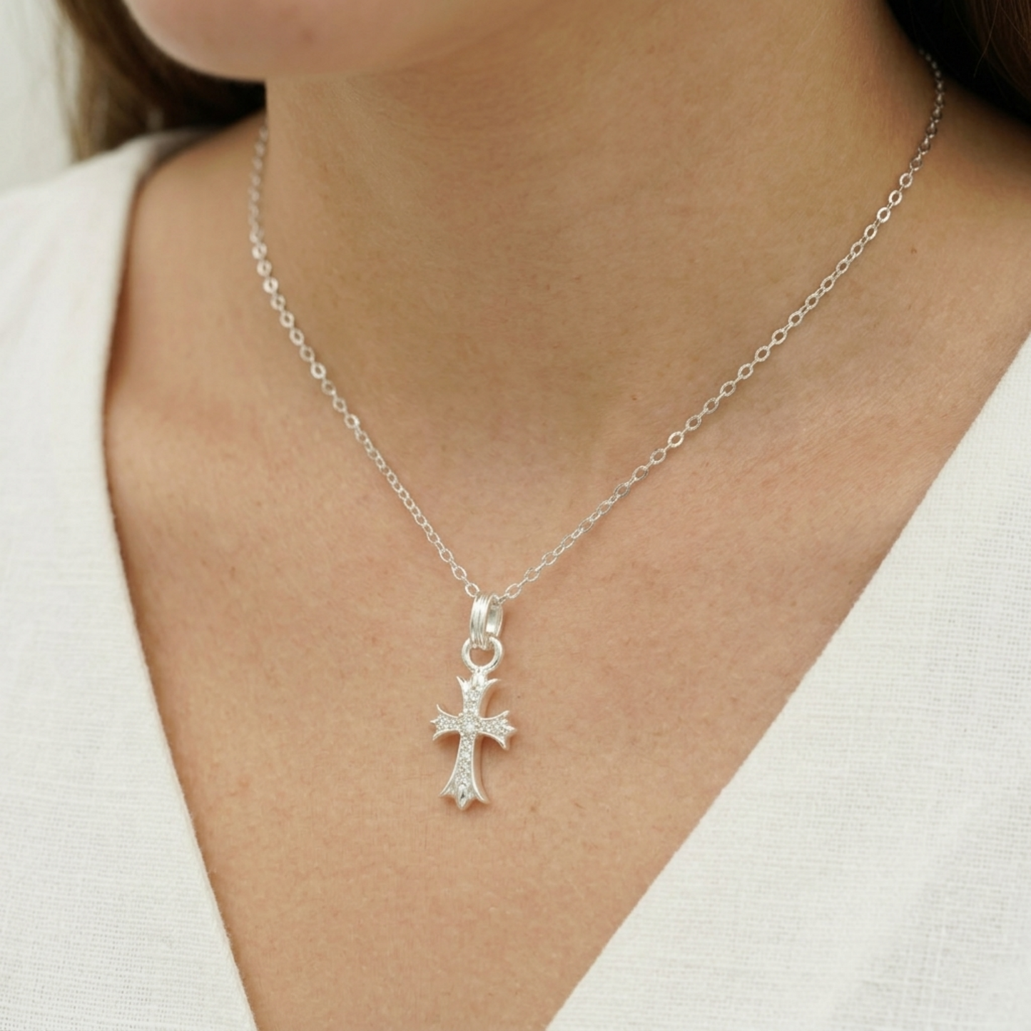 Silver CZ cross pendant on a chain necklace, shown at the neckline