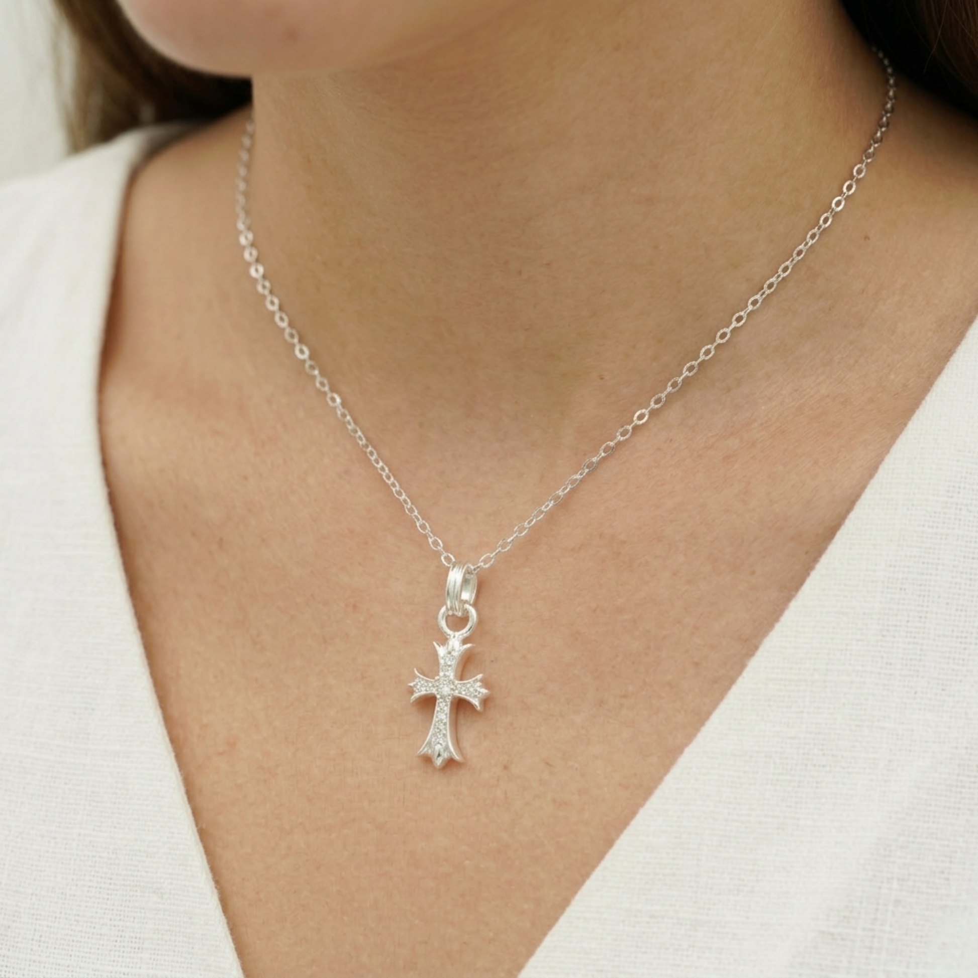 Silver CZ cross pendant on a chain necklace, shown at the neckline