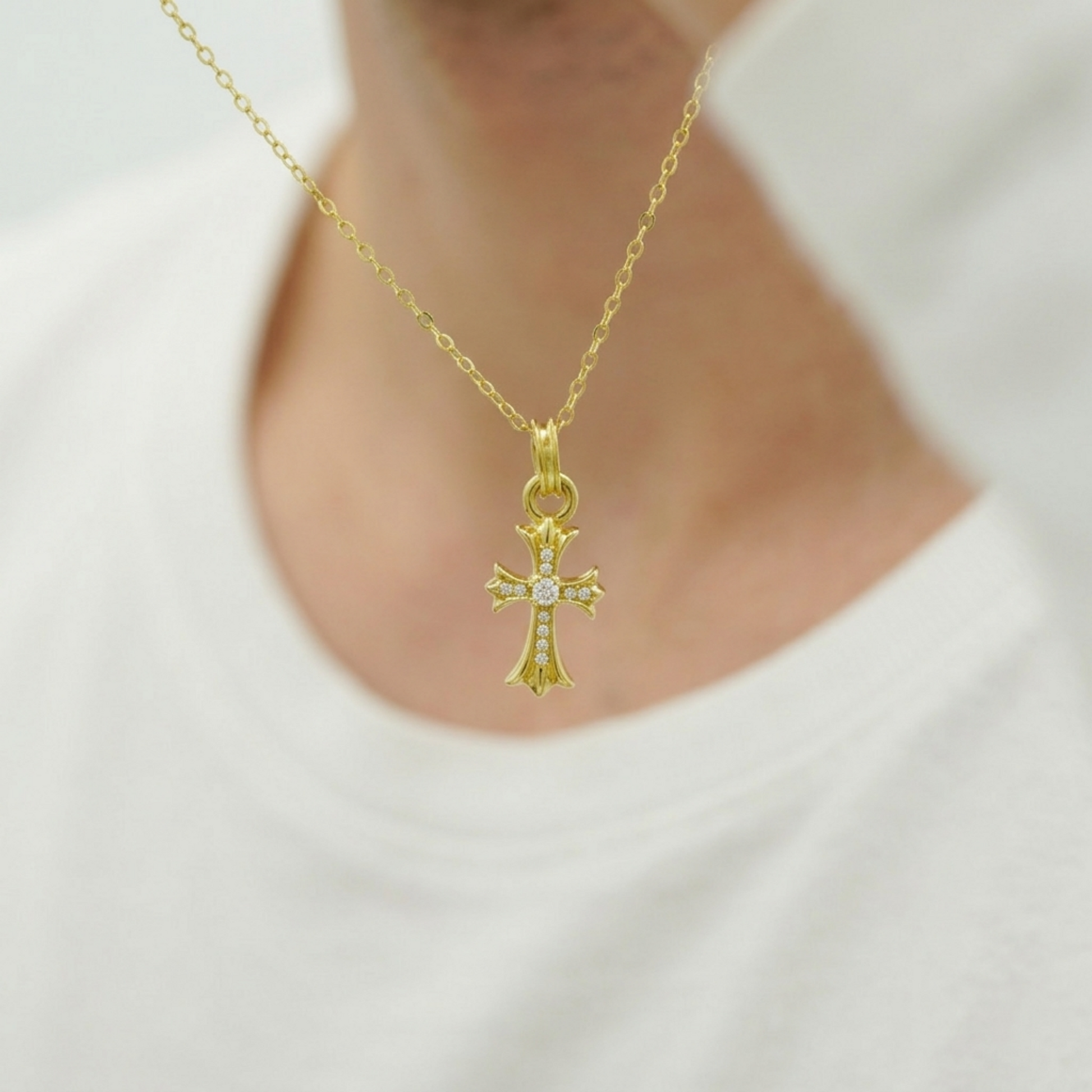 Gold CZ cross pendant on a chain necklace, shown on a person’s chest