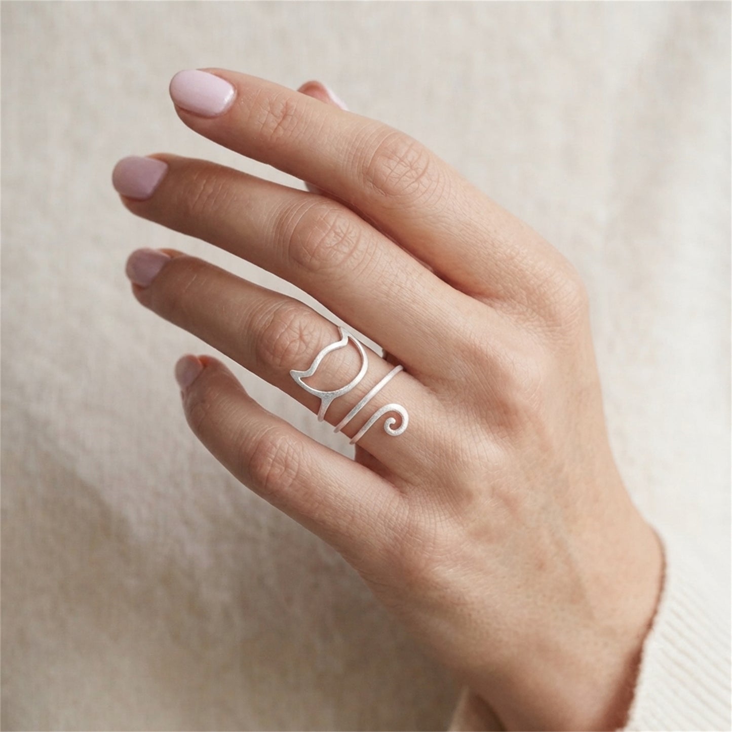 Kitten wraparound ring on hand, silver-tone cat-face motif with curly tail detail.