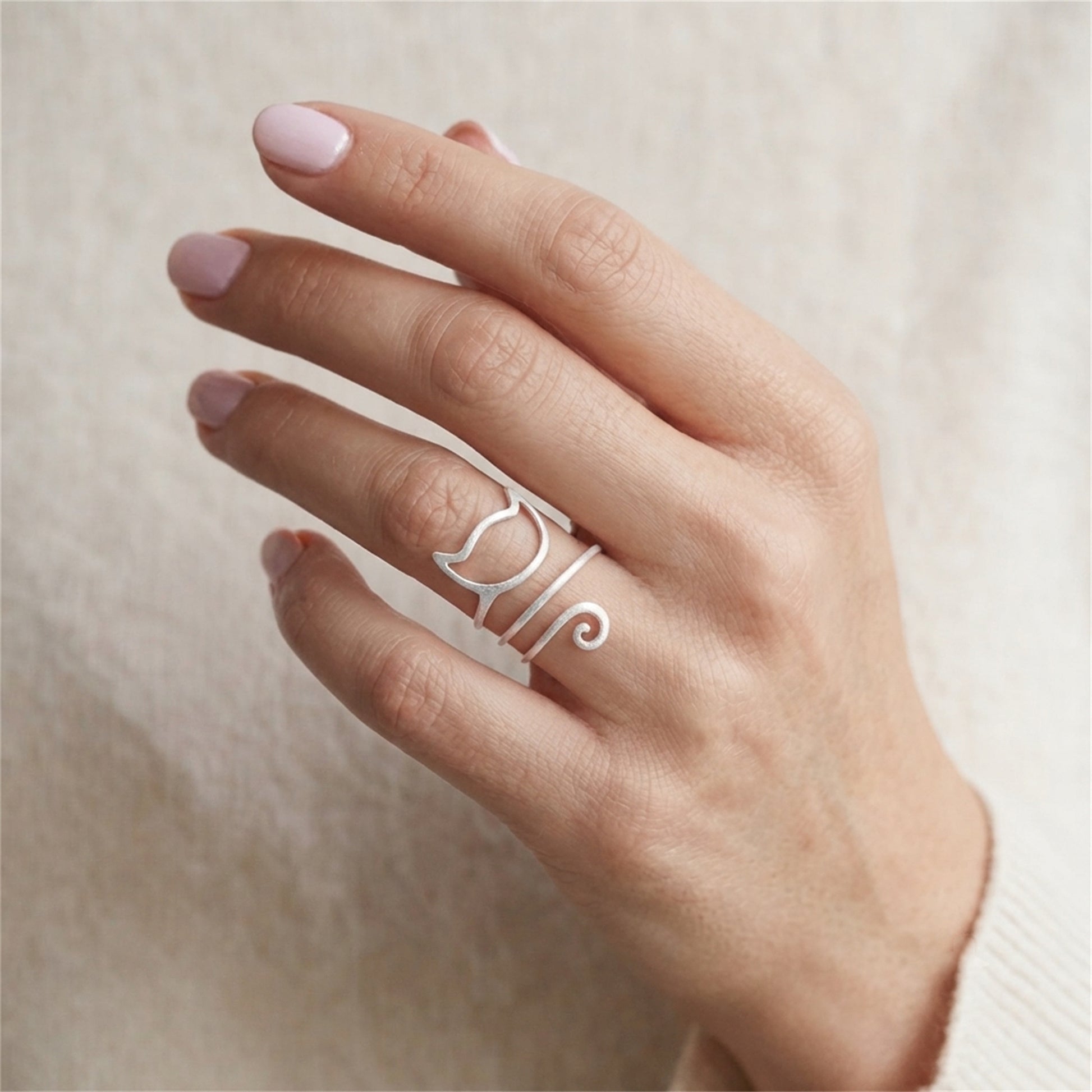 Kitten wraparound ring on hand, silver-tone cat-face motif with curly tail detail.