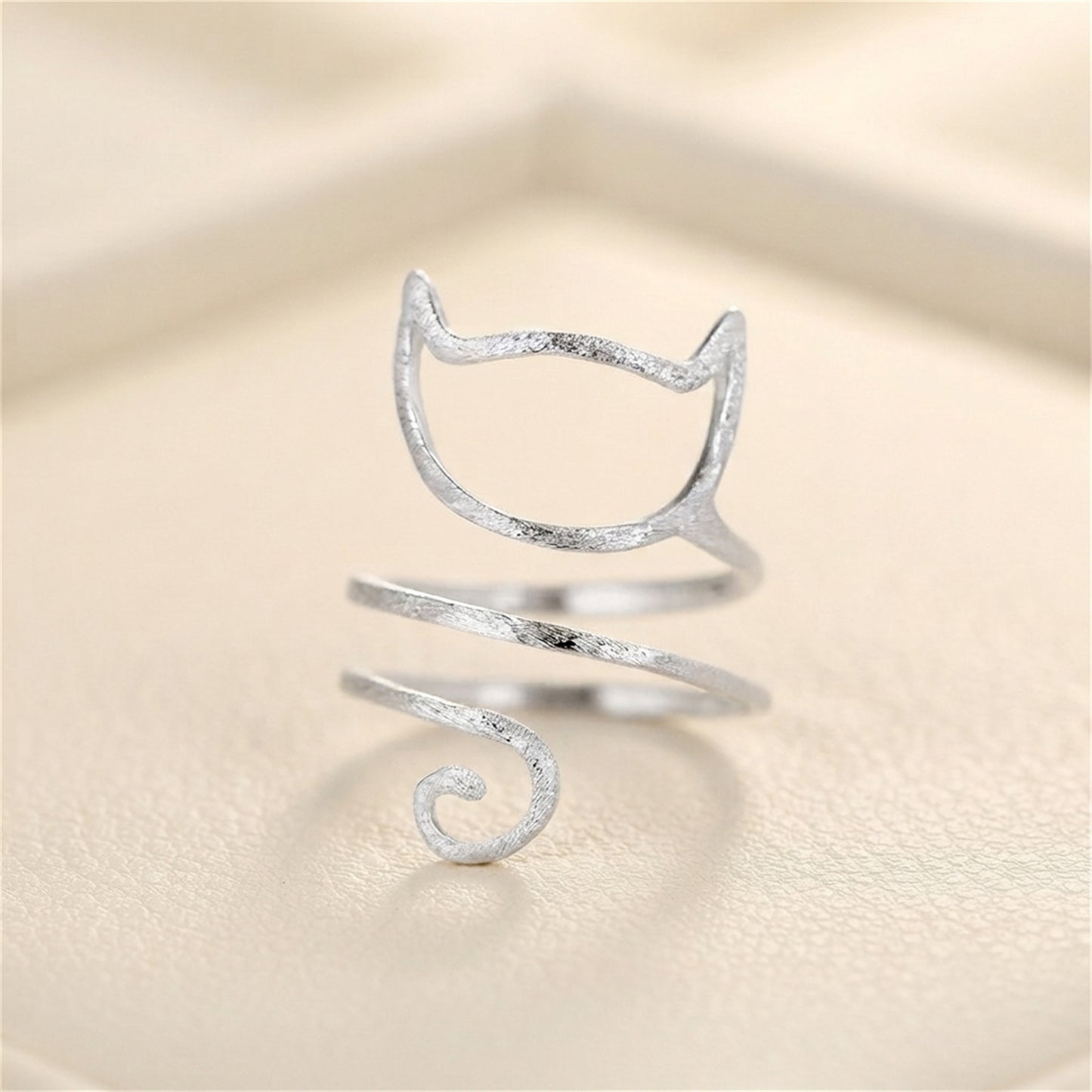 Silver-tone kitten wraparound ring on fabric, cat-face design with spiral tail.