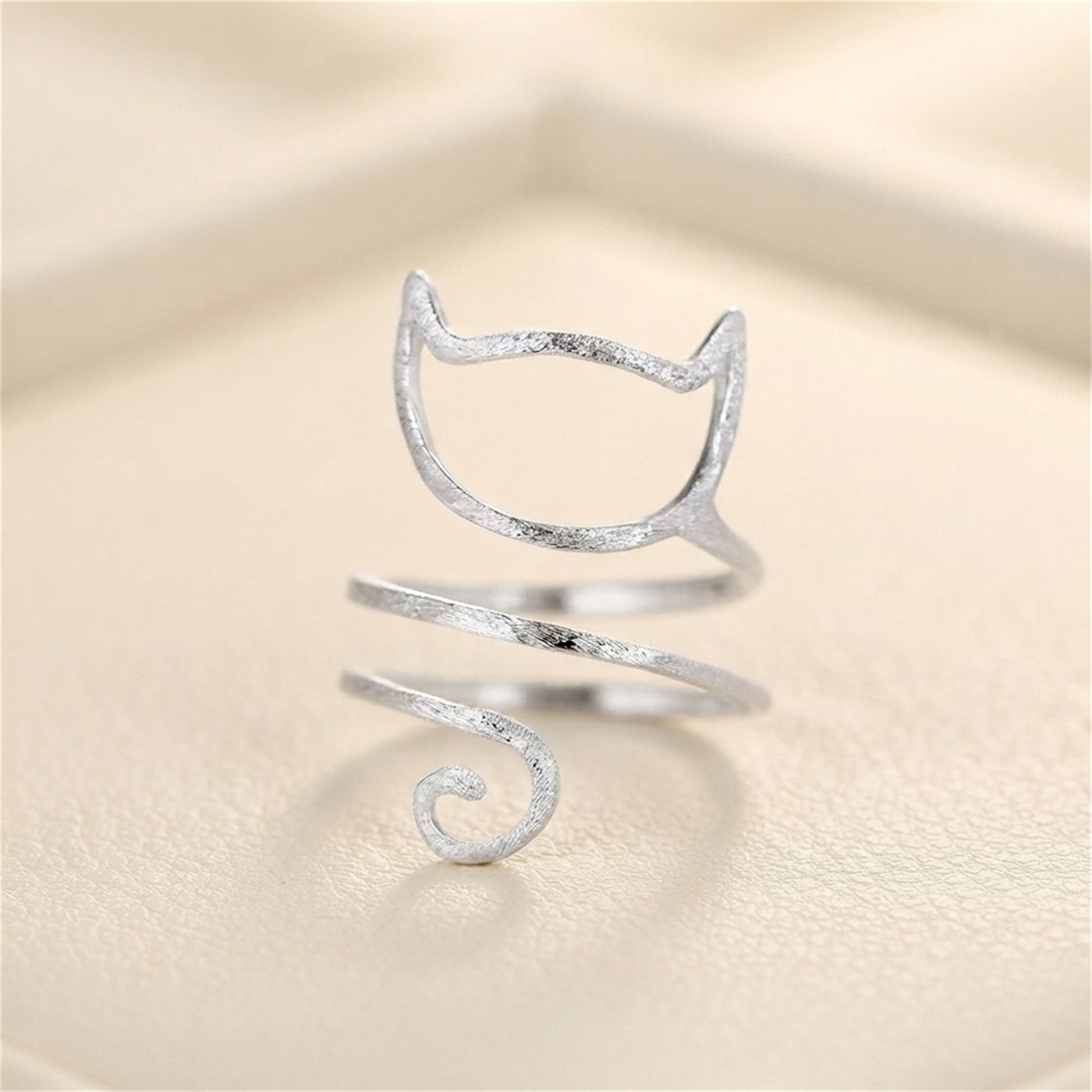 Silver-tone kitten wraparound ring on fabric, cat-face design with spiral tail.