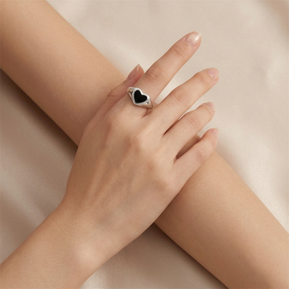 Black heart ring on finger, silver-tone wishbone band with black enamel heart